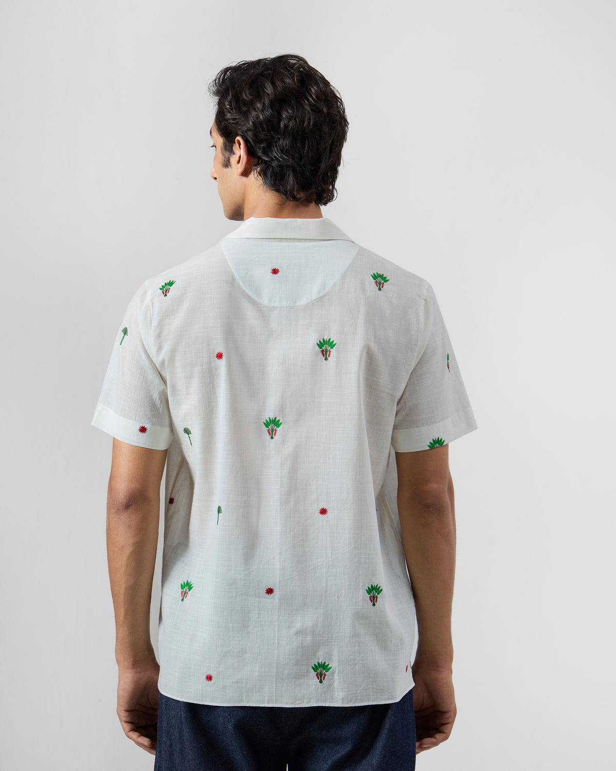 Back of a white Delta Shirt scattered with green palm embroidery.