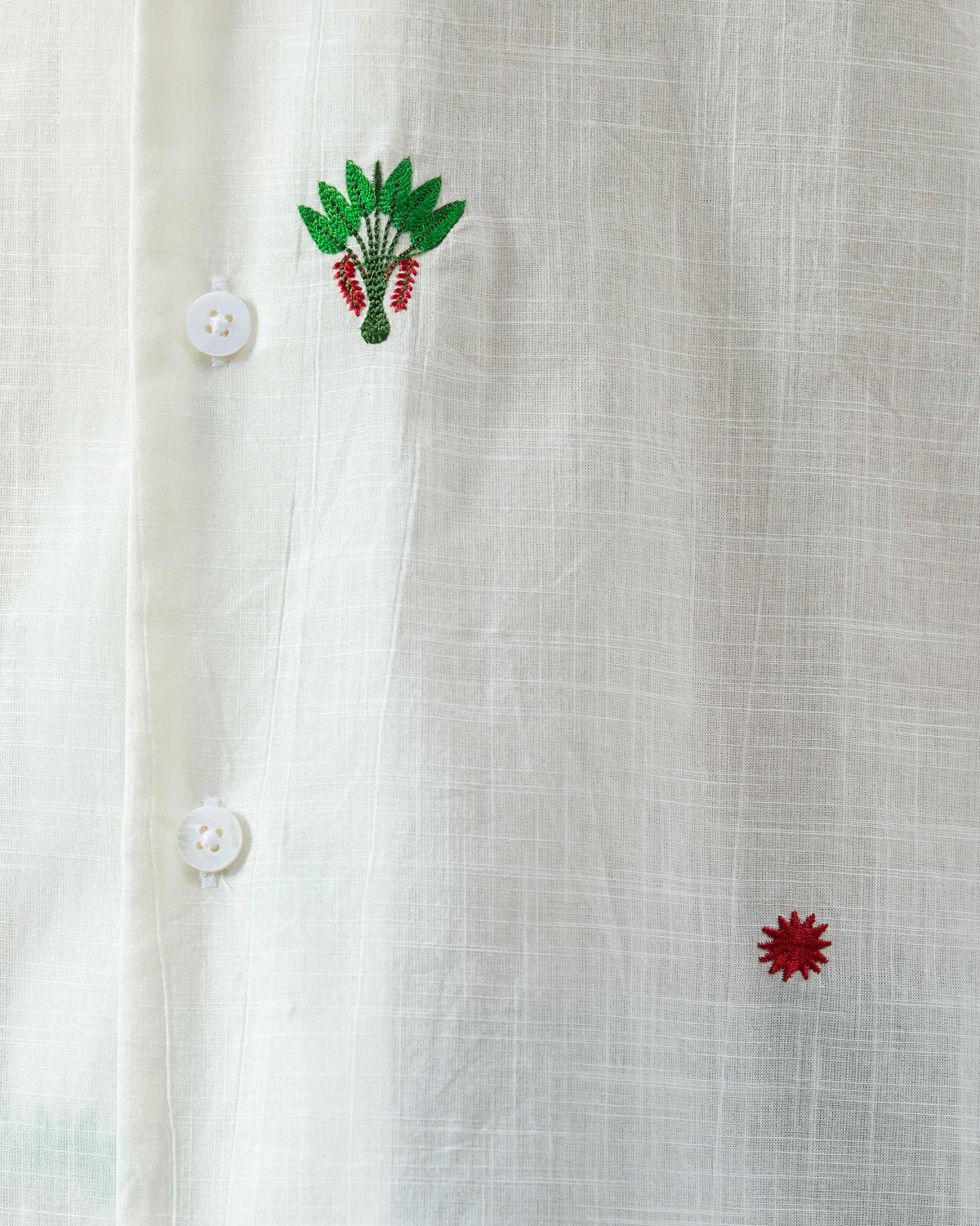 Close-up of a white Delta Shirt showing green palm embroidery on textured cotton.