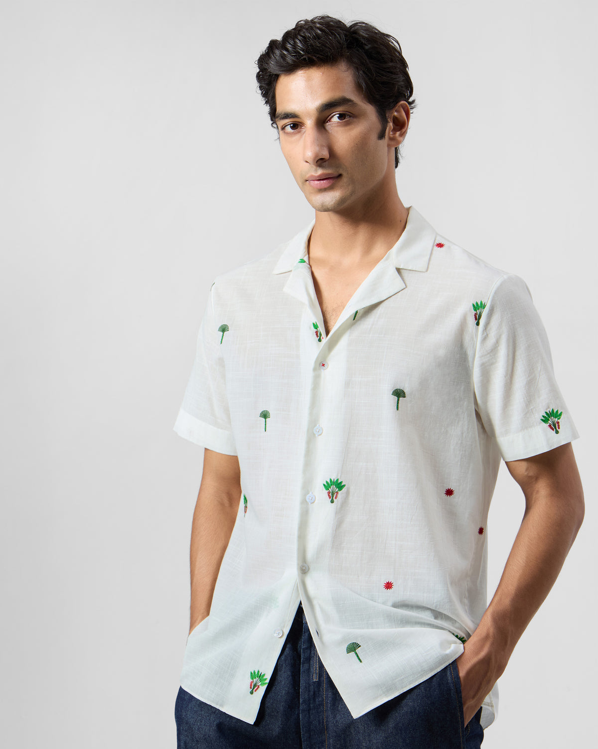 Person wearing a white Delta Shirt with a camp collar and scattered palm embroidery.