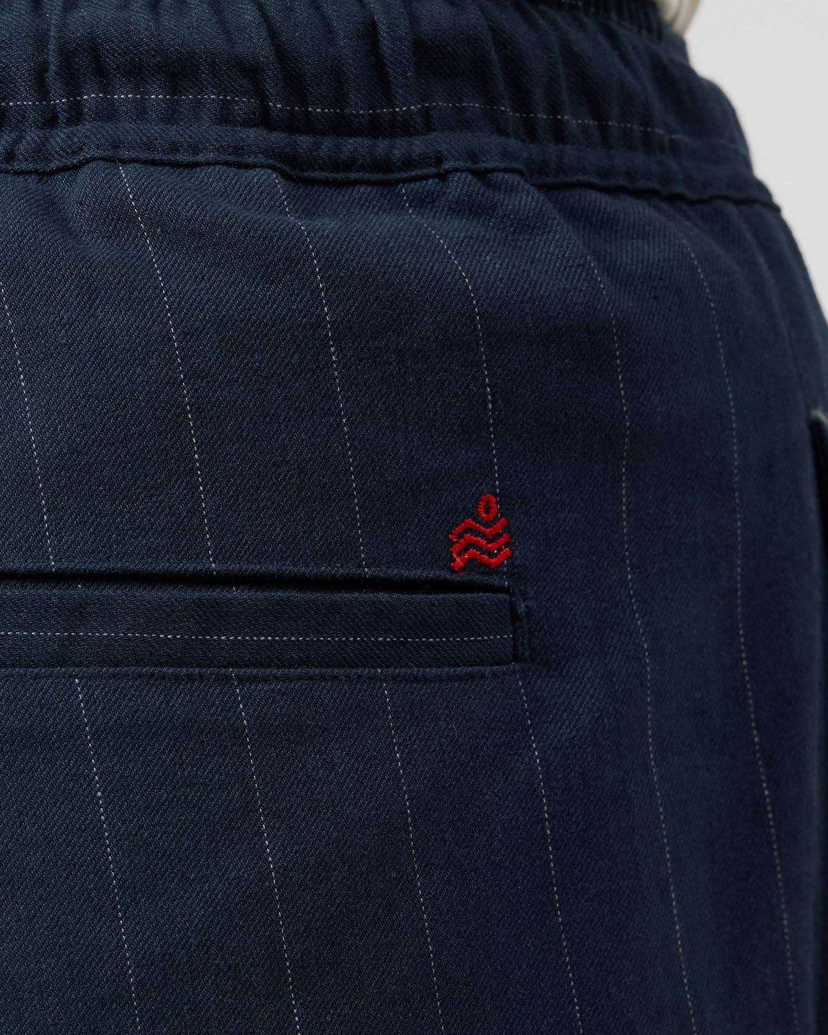Close-up of a navy Vera trouser rear pocket with a red logo.