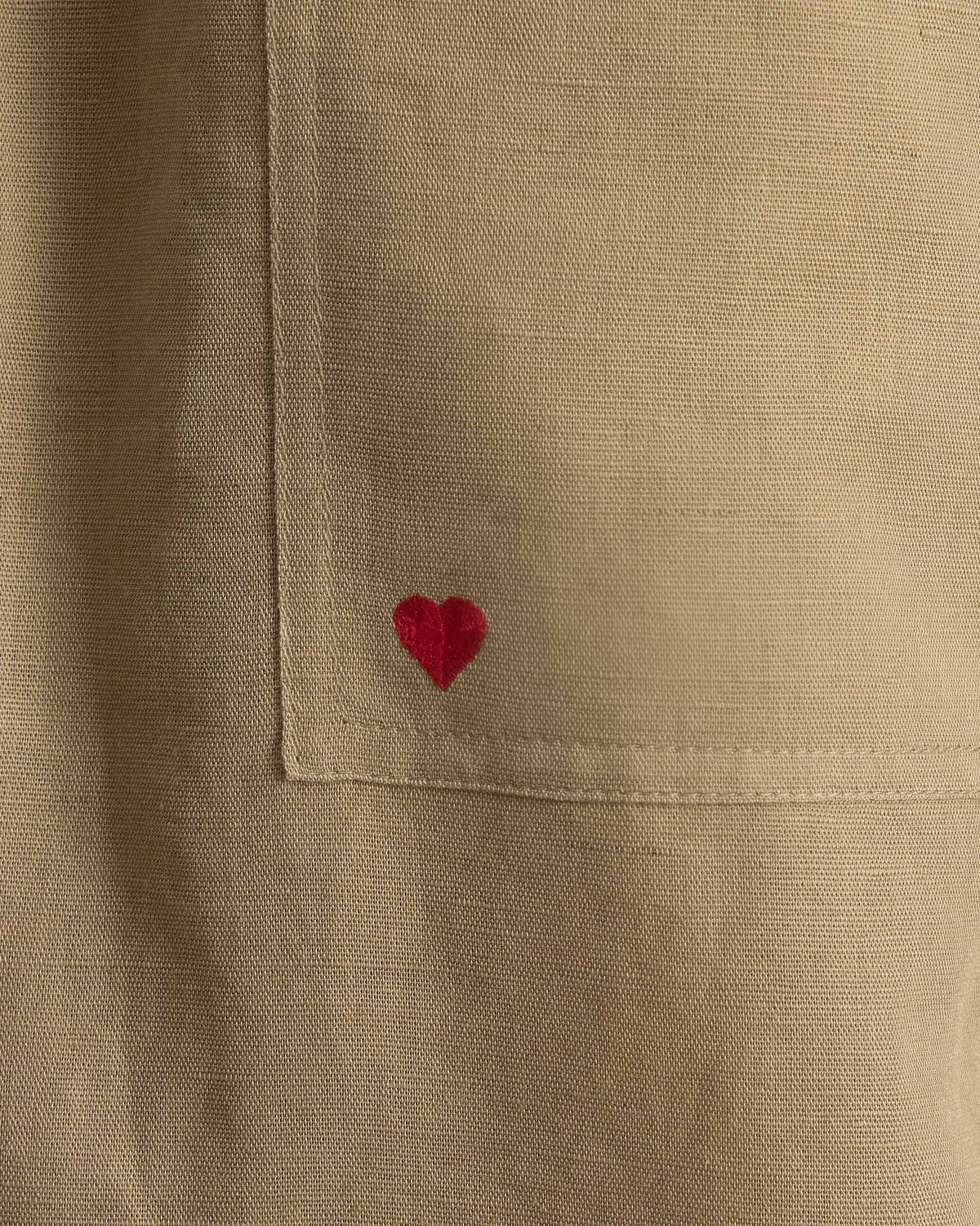 Close-up of taupe Yoka Trousers pocket with a small red heart embroidered on it.