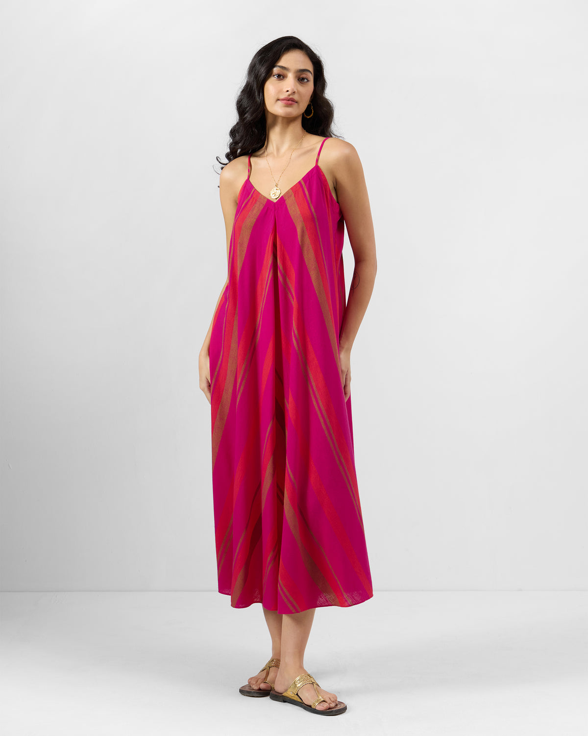 Person wearing a pink and orange striped Narali strappy dress with a flared midi shape.
