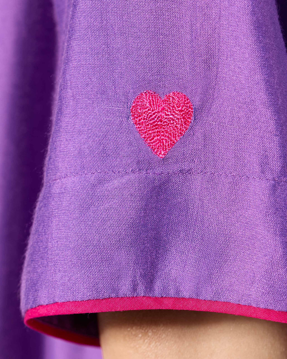 Close-up of a pink embroidered heart and magenta cuff on a purple Happy Heart Dress sleeve.