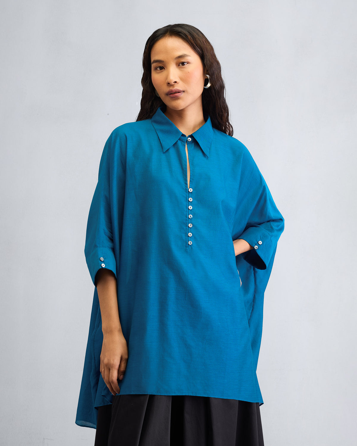 Person wearing a sapphire Hala tunic with wide sleeves and a white button placket.