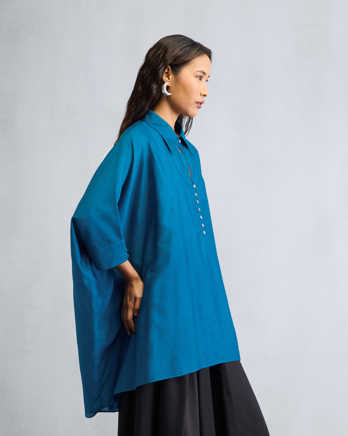 Side view of a sapphire Hala tunic showing its oversized draped silhouette.