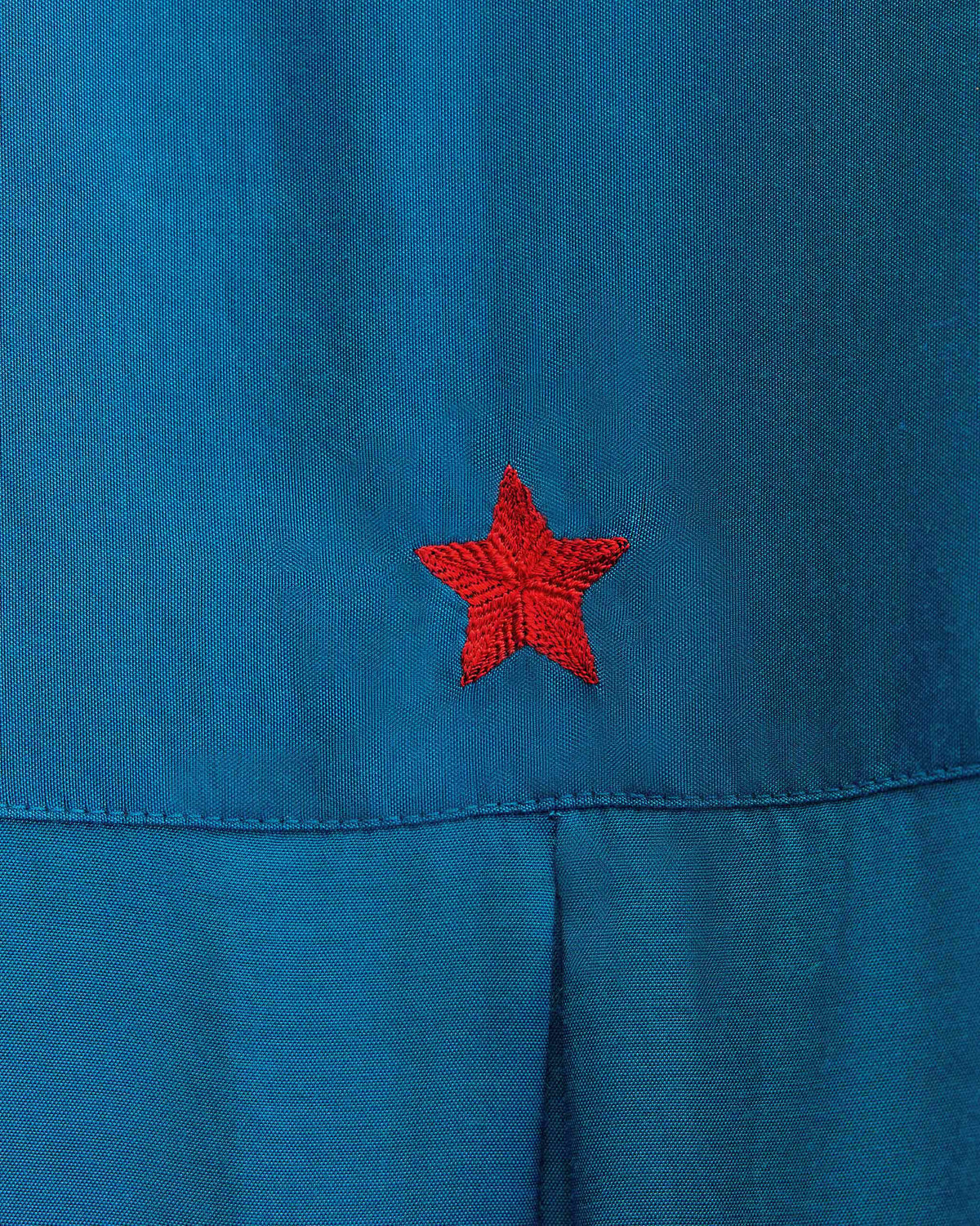 Close-up of a red embroidered star on a teal Lazy Sunday tunic.