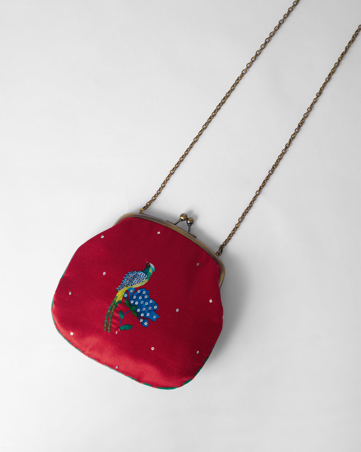 Red sling clutch with an embroidered blue bird, kiss-lock frame, and chain strap.