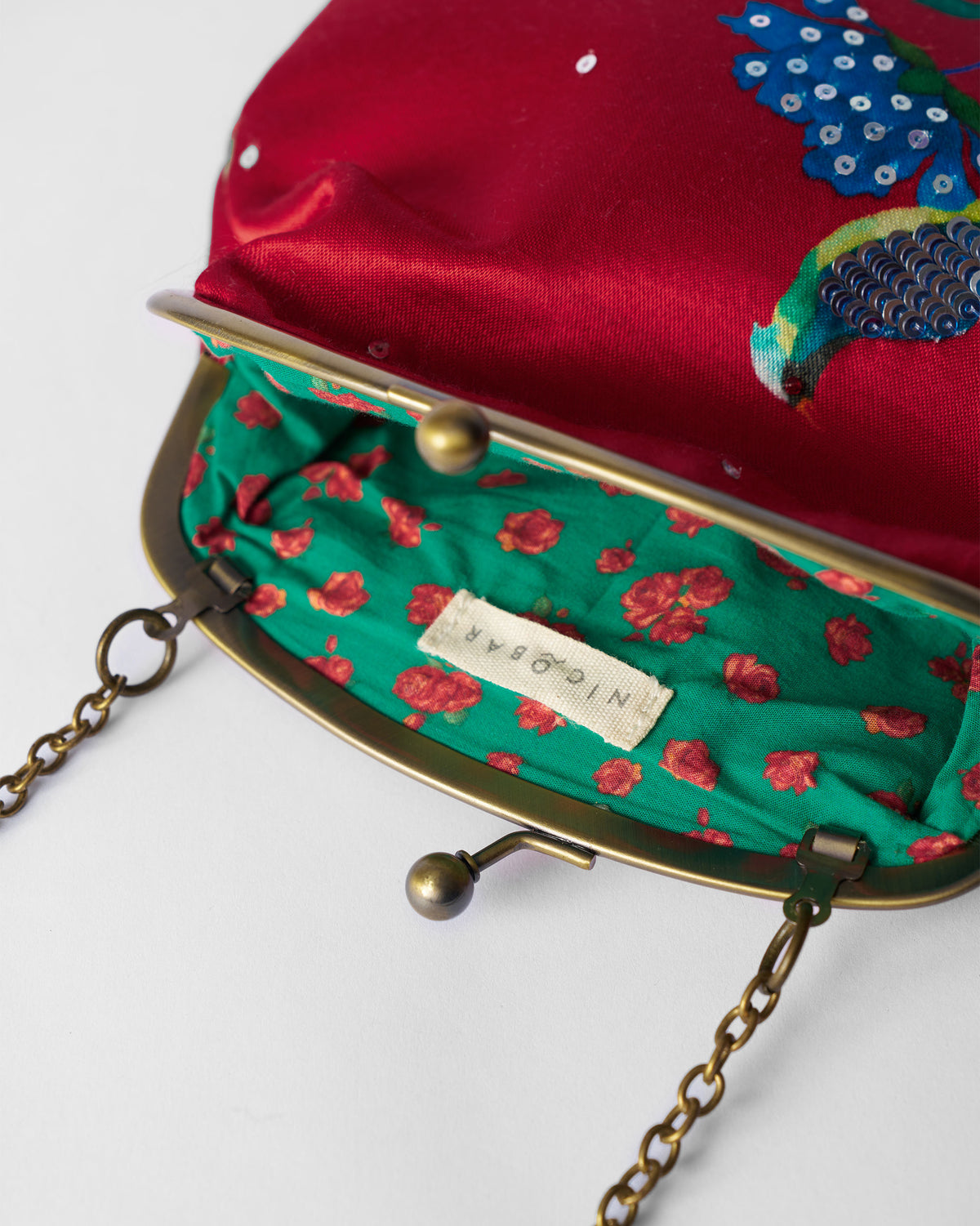 Open red embroidered clutch showing green rose lining and brass kiss-lock.