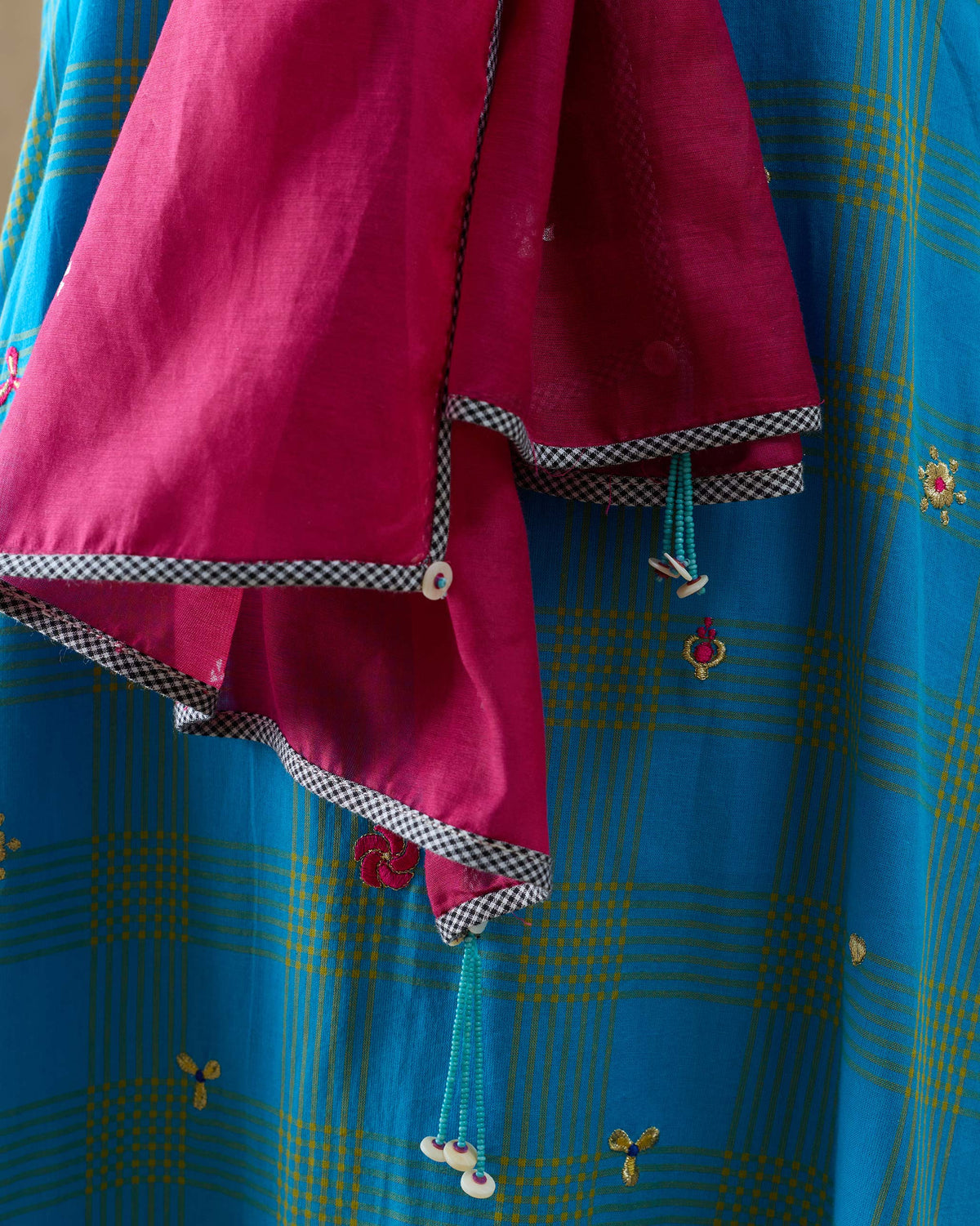 Close-up of a Jashn scarf edge showing a checked border and beaded tassels.