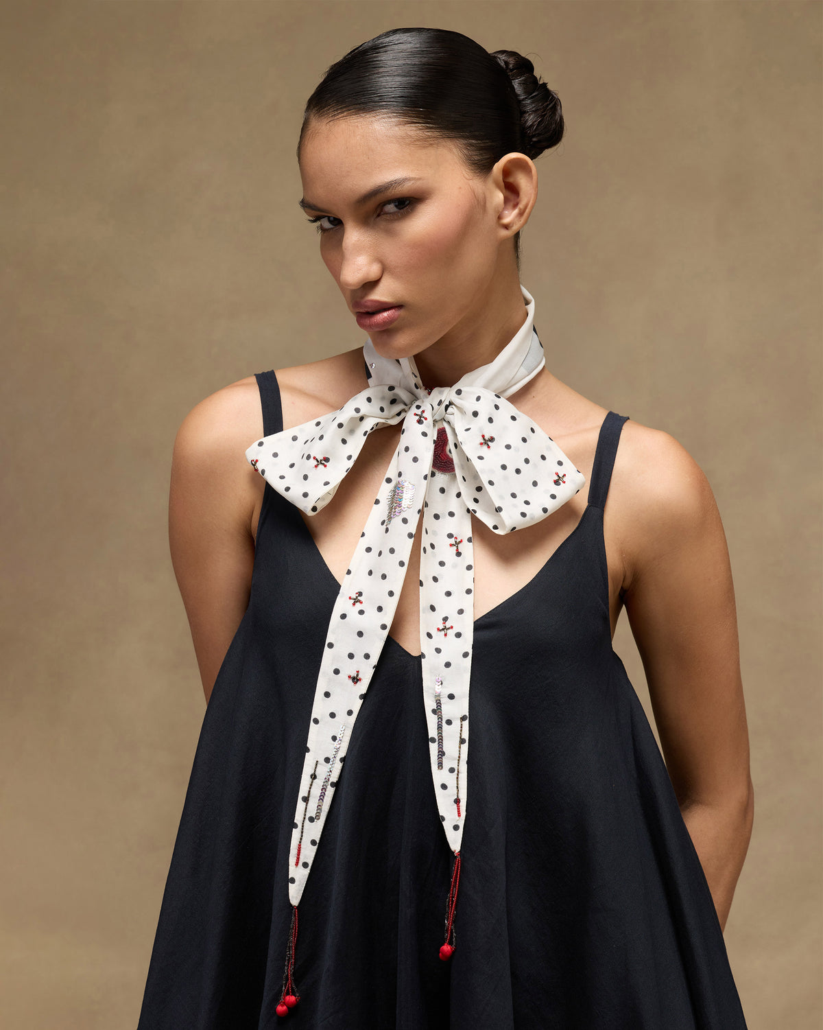 Ivory polka-dot scarf tied in a bow at the neck with red beaded tassels.