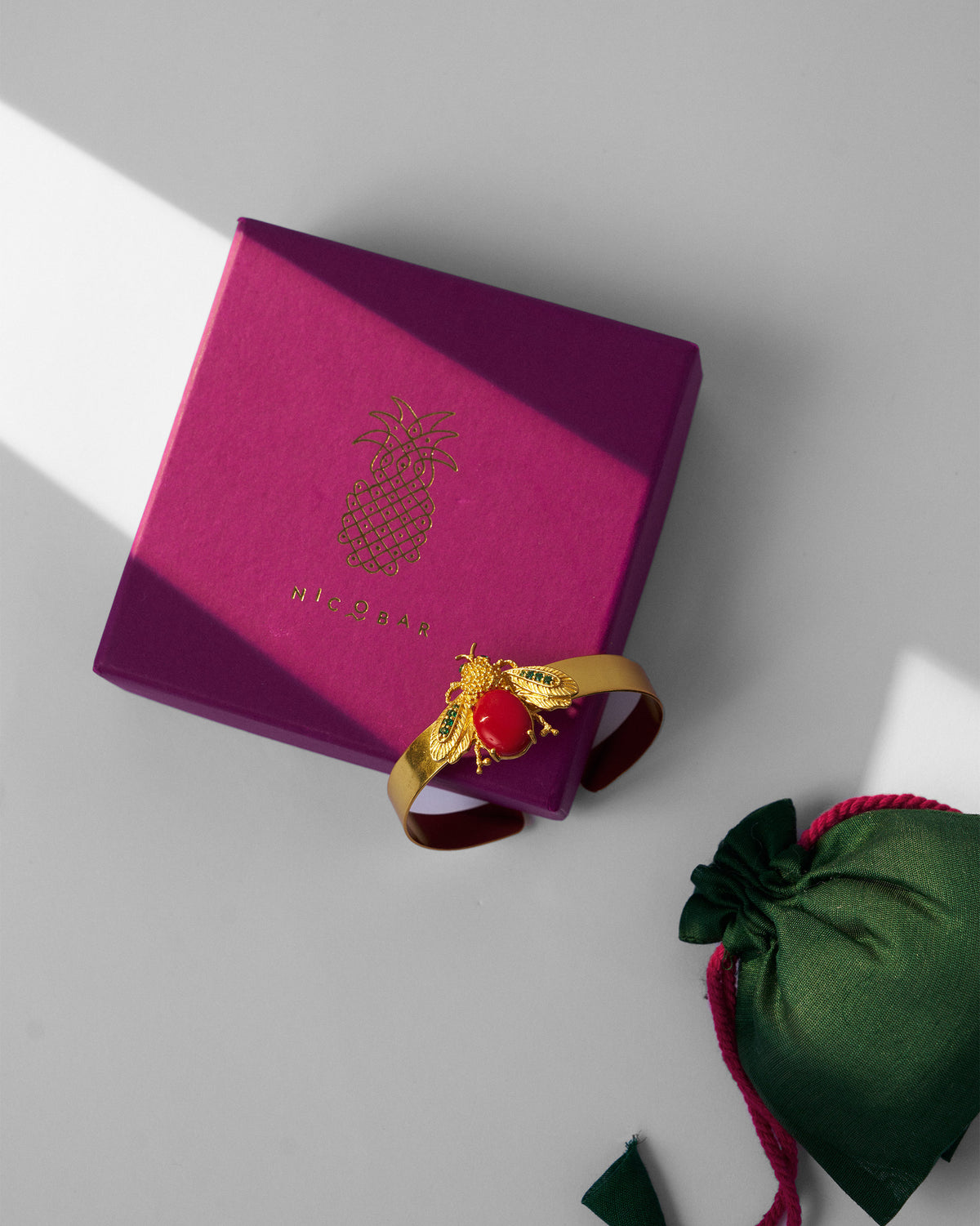 Gold Bug bracelet with a magenta Nicobar gift box and green pouch.