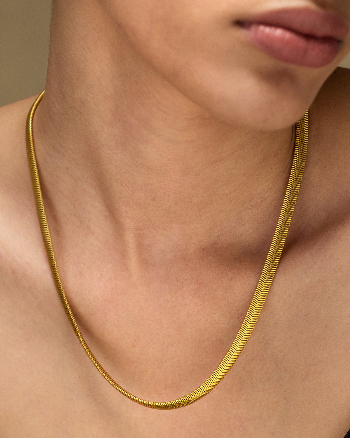 Gold herringbone chain draped at the collarbone.