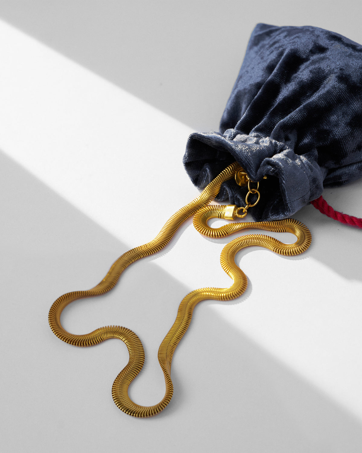 Gold herringbone chain spilling from a navy velvet pouch.
