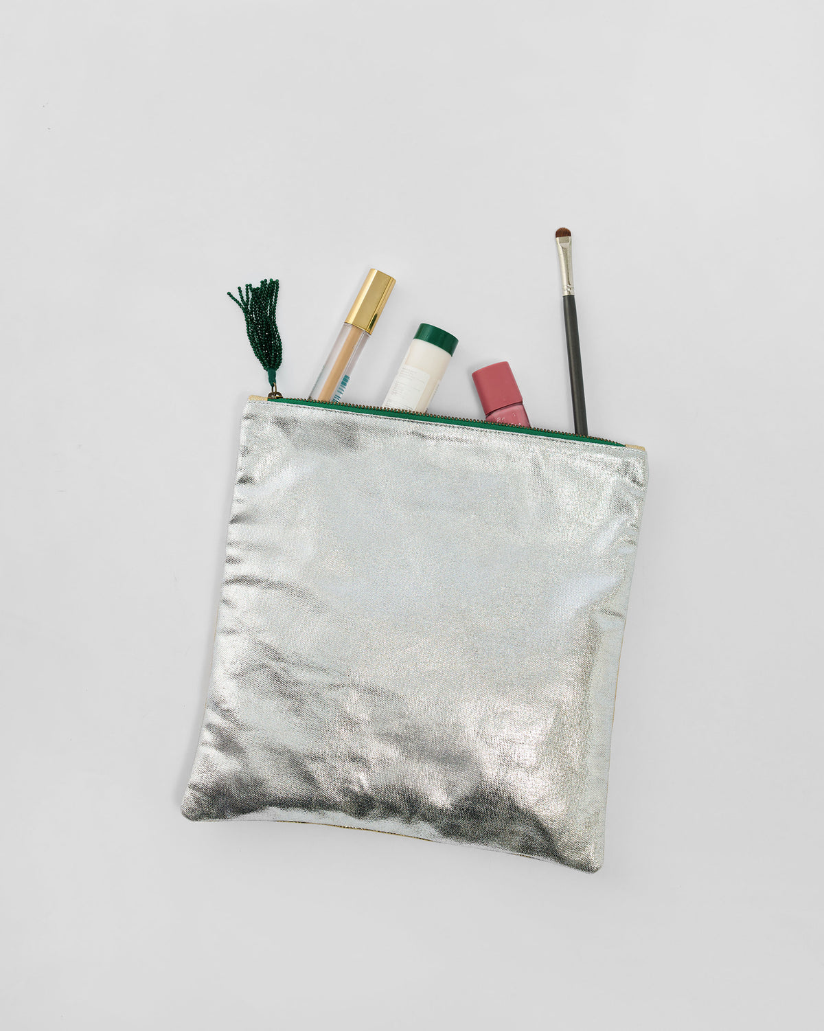 Open silver Fold Over Clutch with a green zipper holding makeup.
