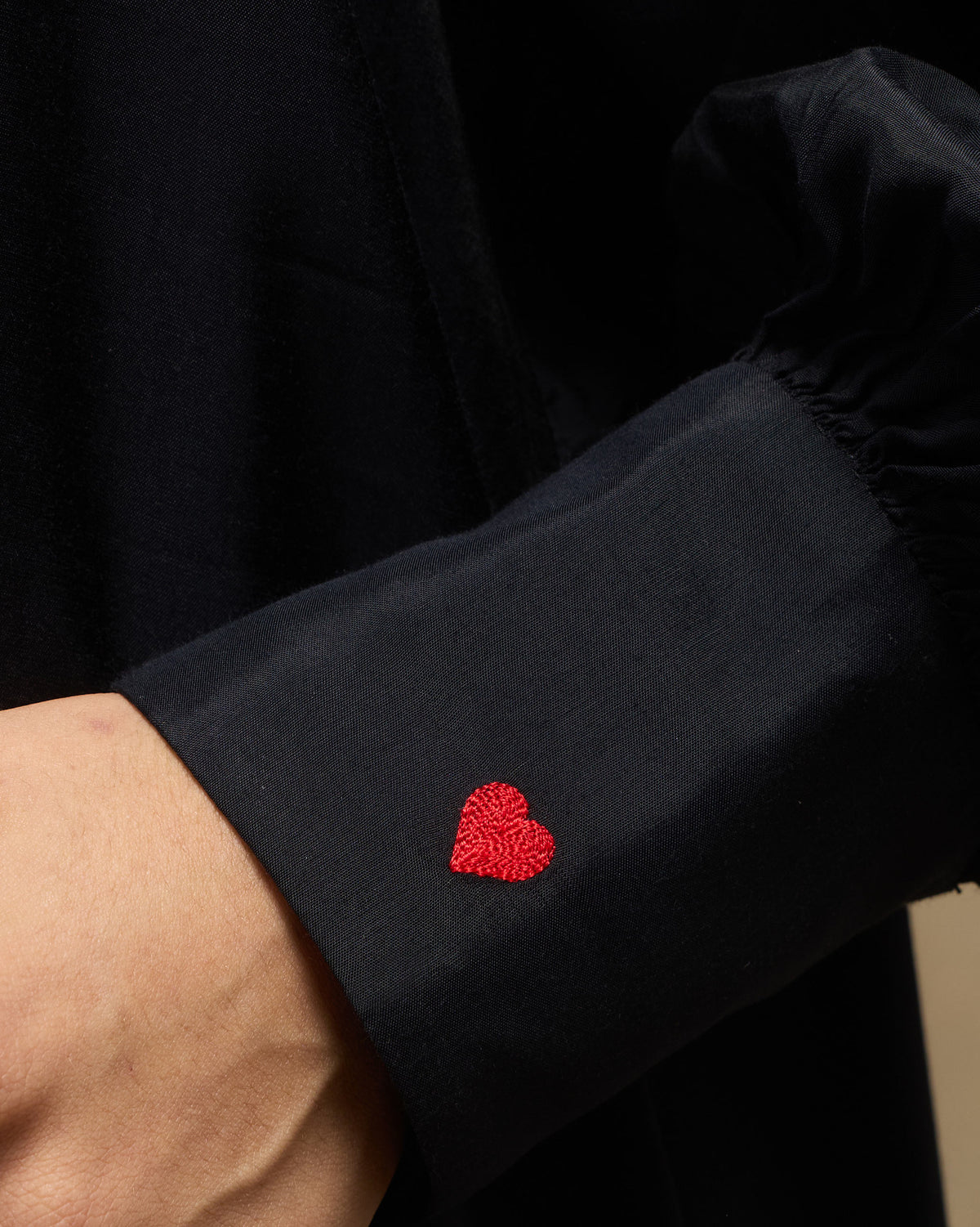 Close-up of a black sleeve cuff with a red embroidered heart.
