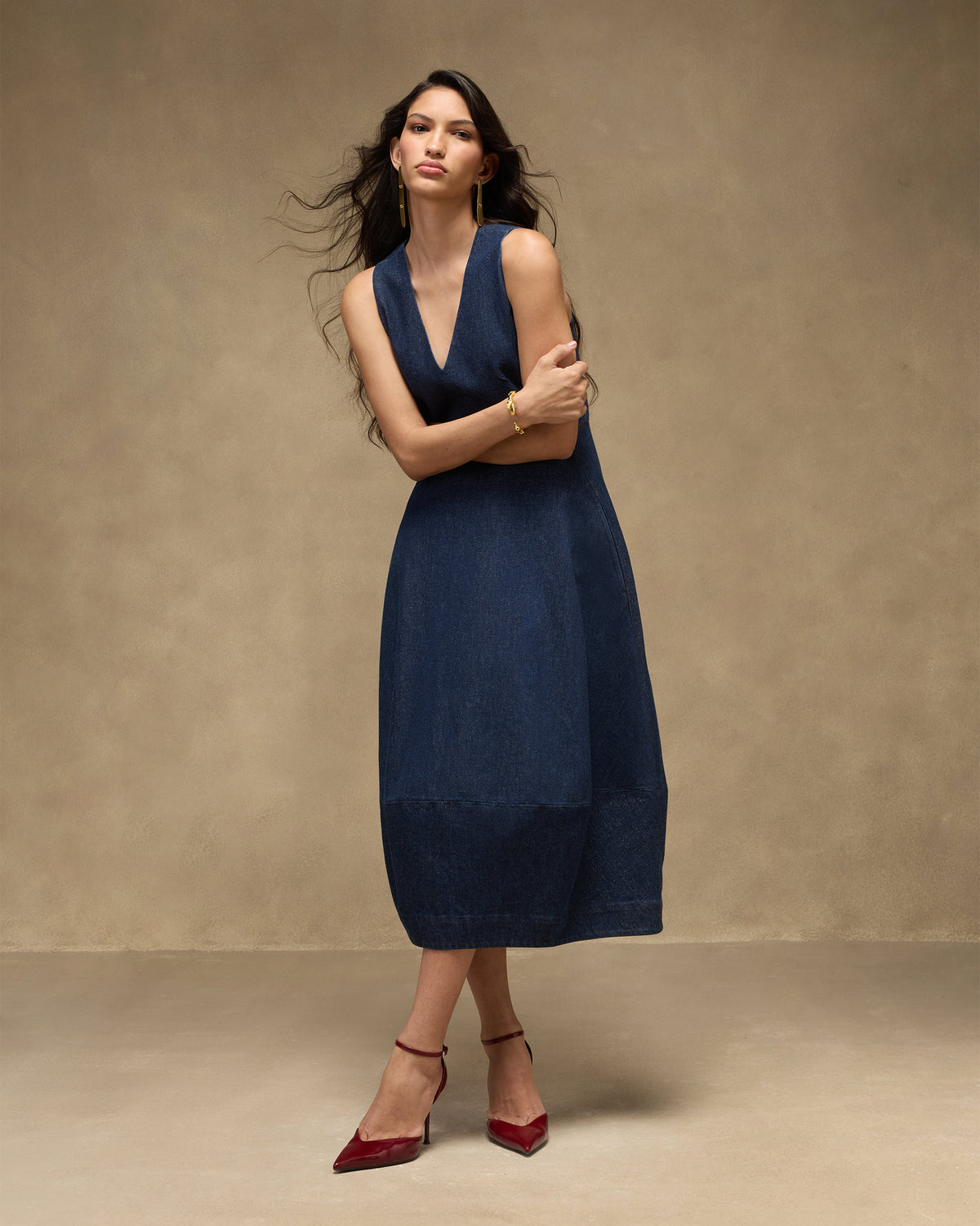 Person wearing a sleeveless navy denim Sway dress with a deep V neckline.