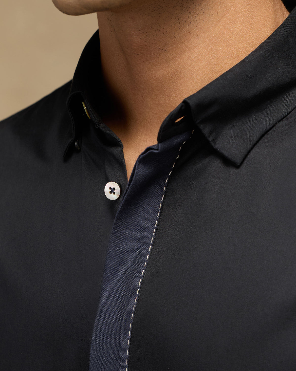 Close-up of a black Midnight Shirt showing navy placket trim and white stitch.