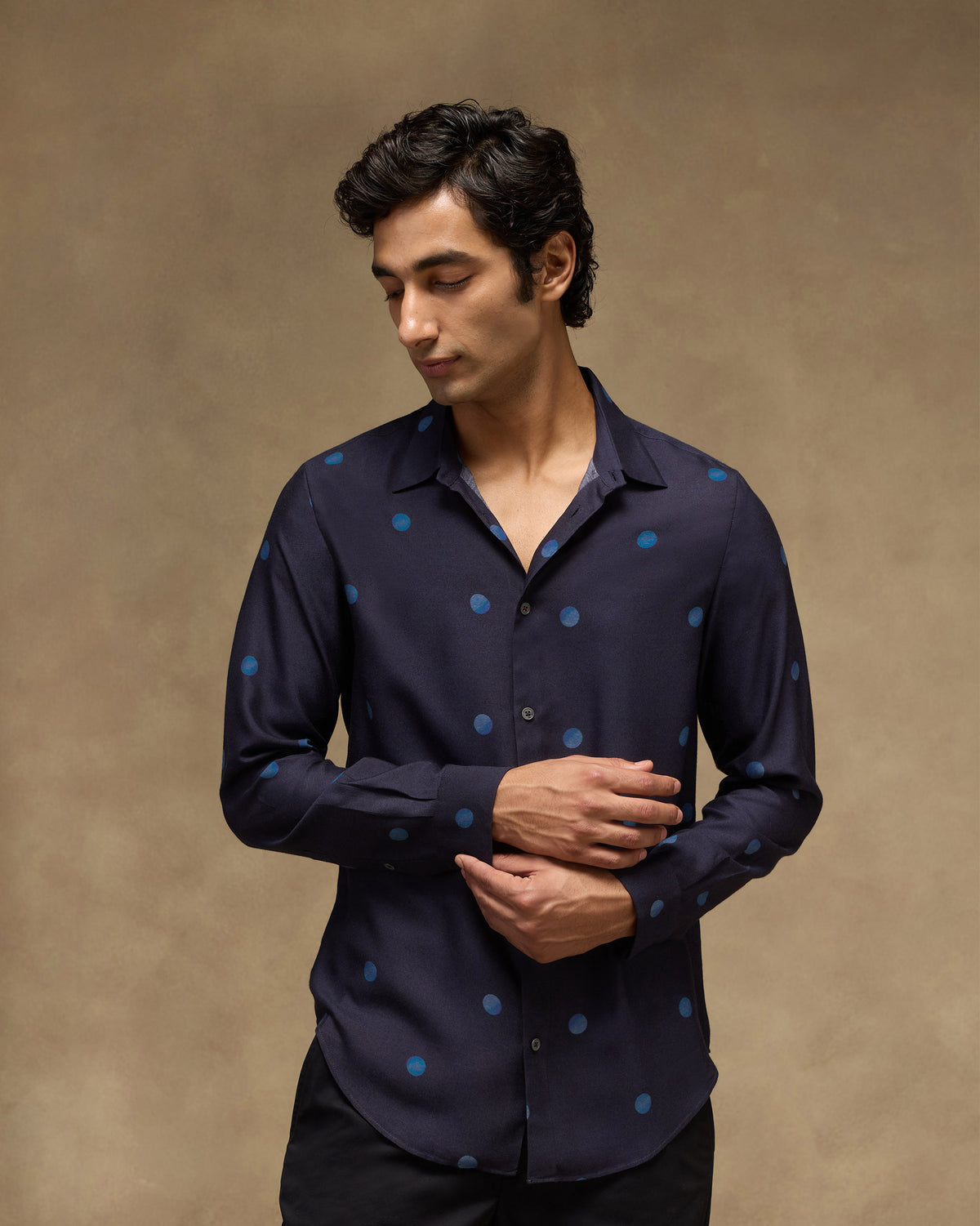 Person adjusting the cuff of a dark navy Daze shirt with blue dots.