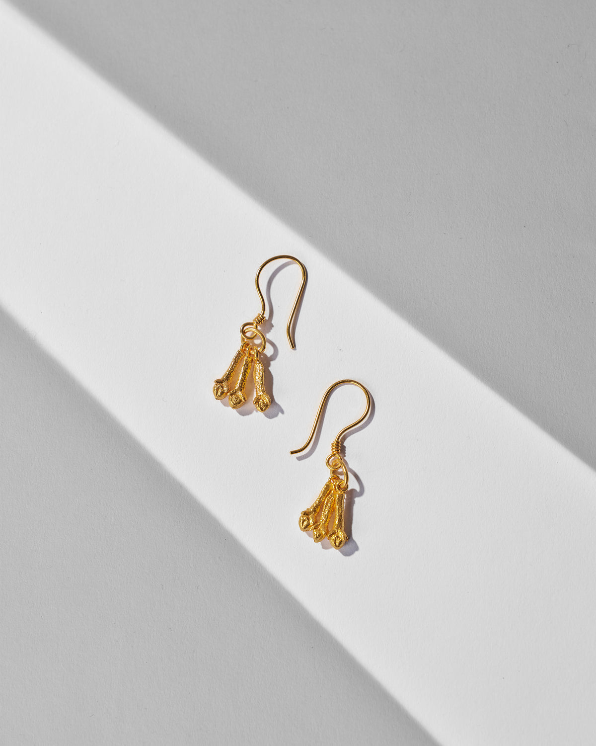 Pair of Clove Earrings laid flat, with gold tapered drops on hook wires.