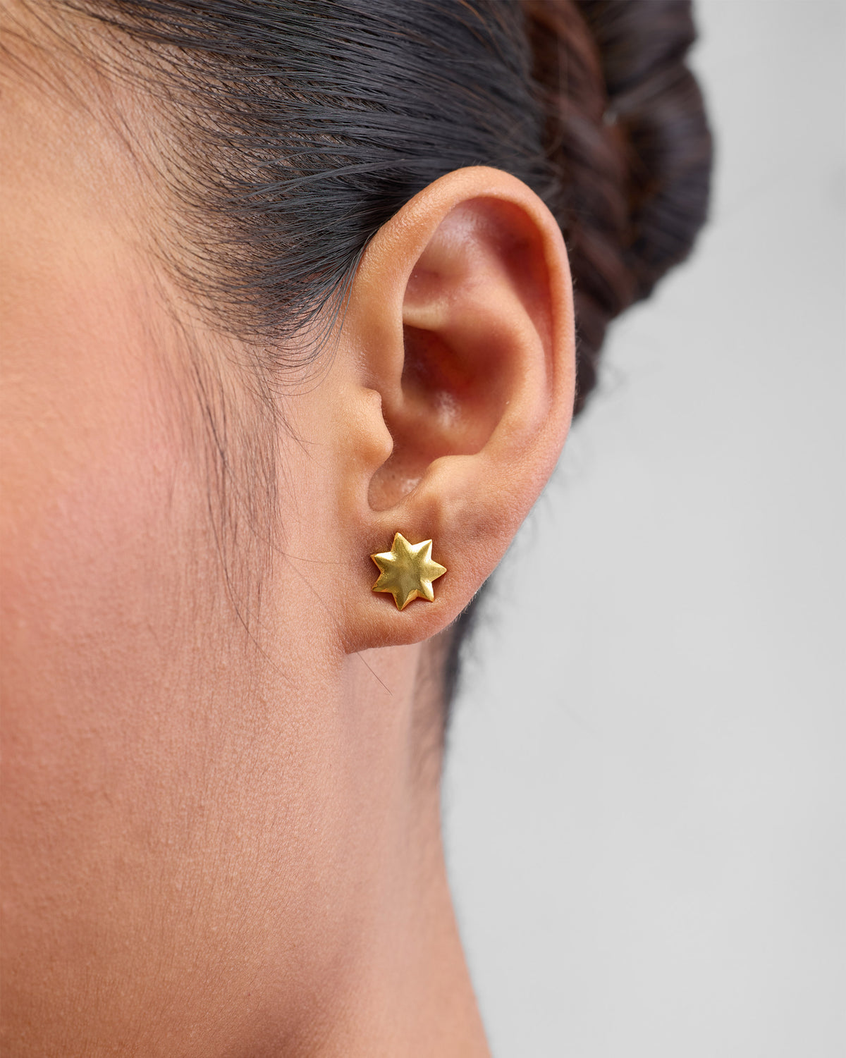 Close-up of gold Sitara Studs worn on an ear, showing the star shape.