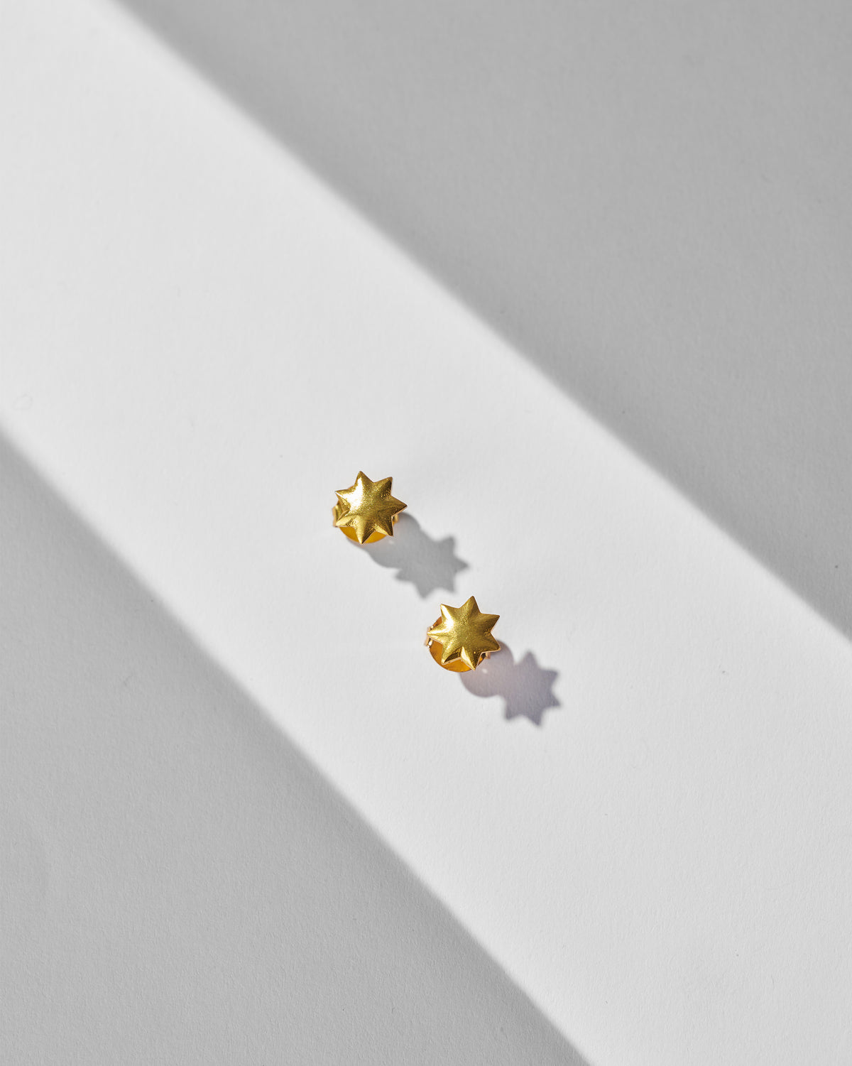 Pair of gold Sitara Studs laid flat.