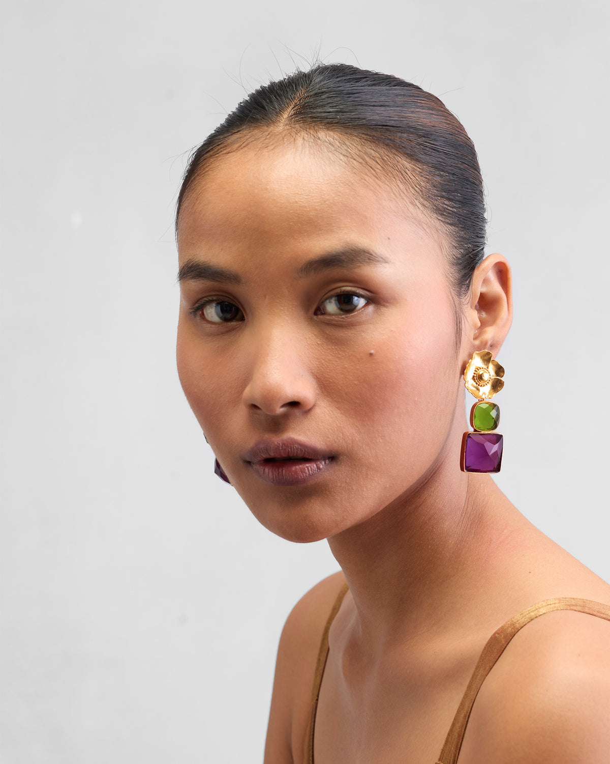 Person wearing gold dessert rose drops with green and purple stones.