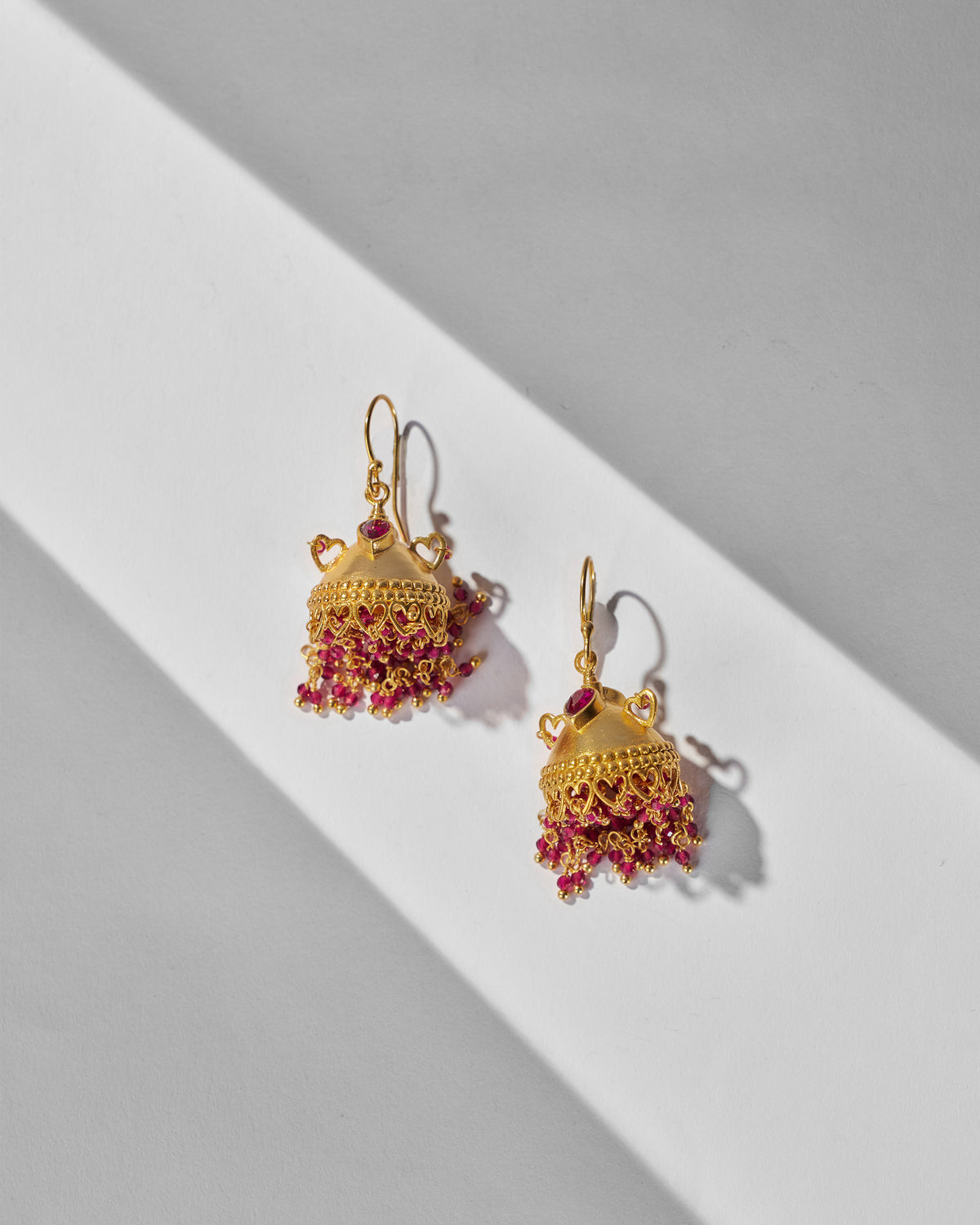 Pair of gold Kaveri jhumkas with heart details and pink beads.