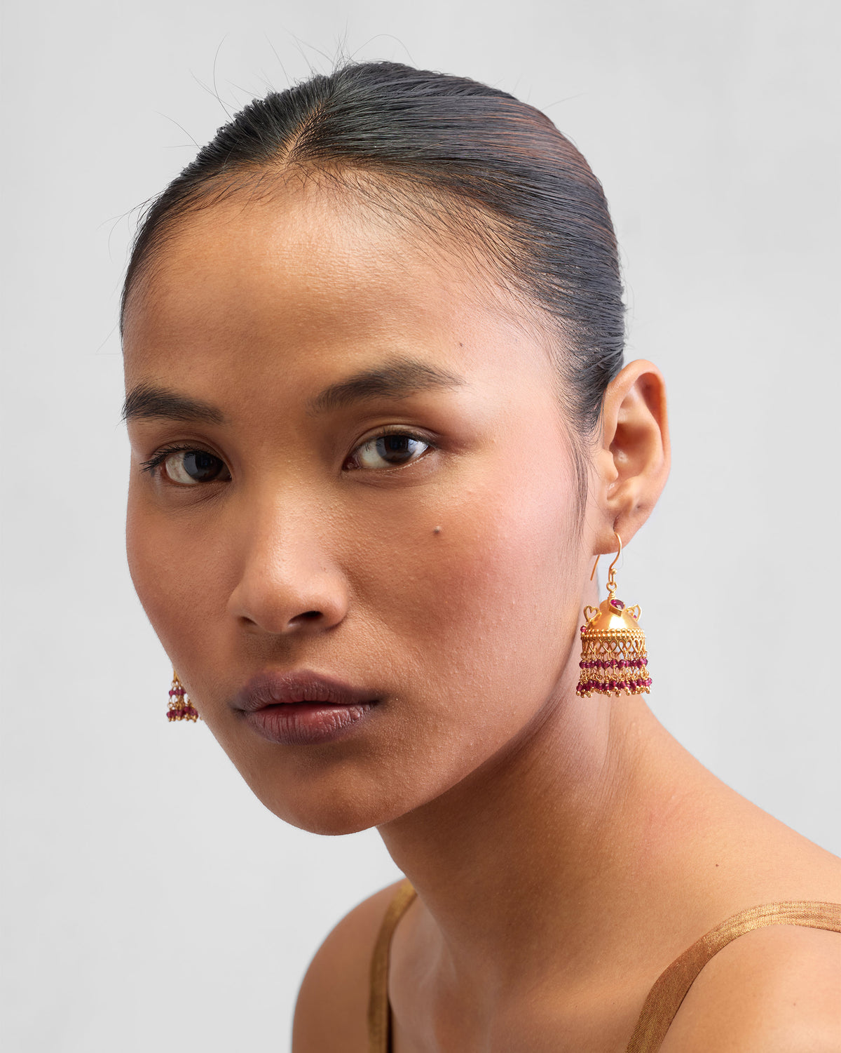 Person wearing gold Kaveri jhumkas with red bead fringe.