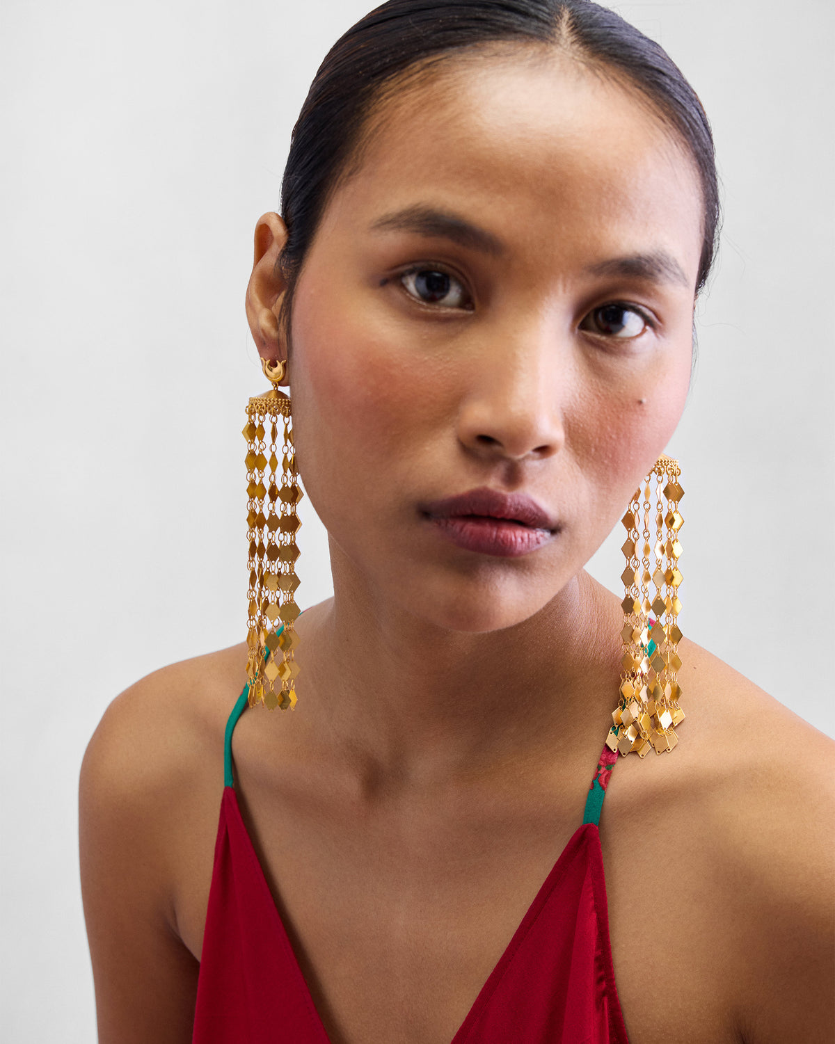 Person wearing long gold Gulbahar earrings with cascading scale fringe.