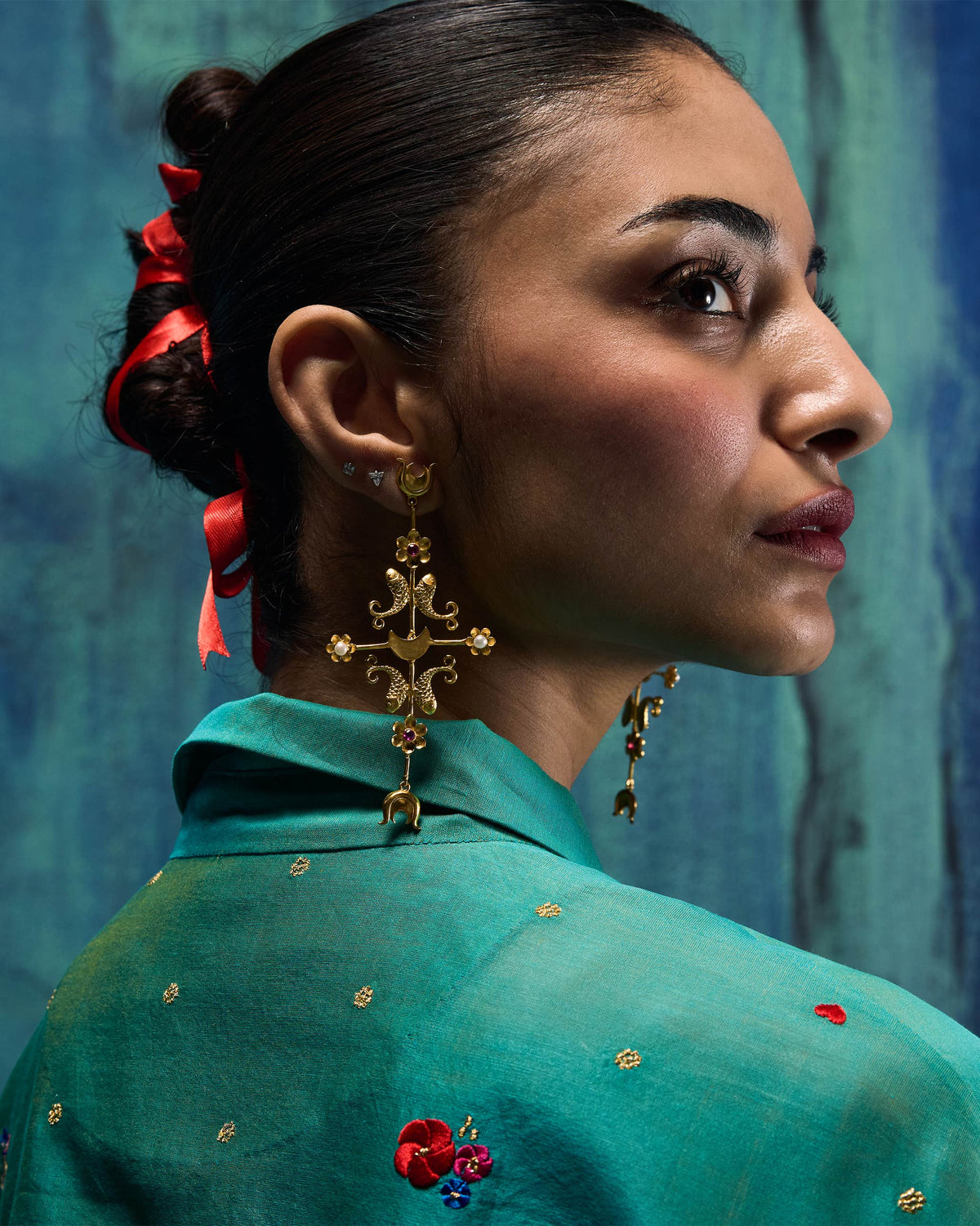 Person wearing a long gold gul baag earring with fish and flower motifs.