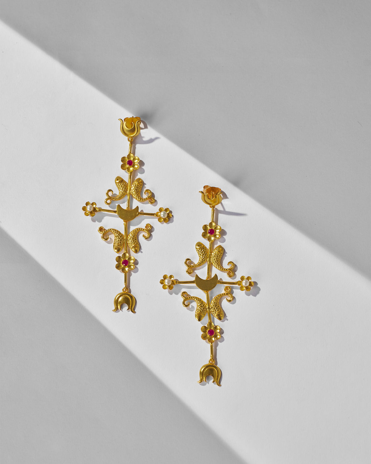 Pair of gold gul baag earrings with fish and flower motifs laid flat.
