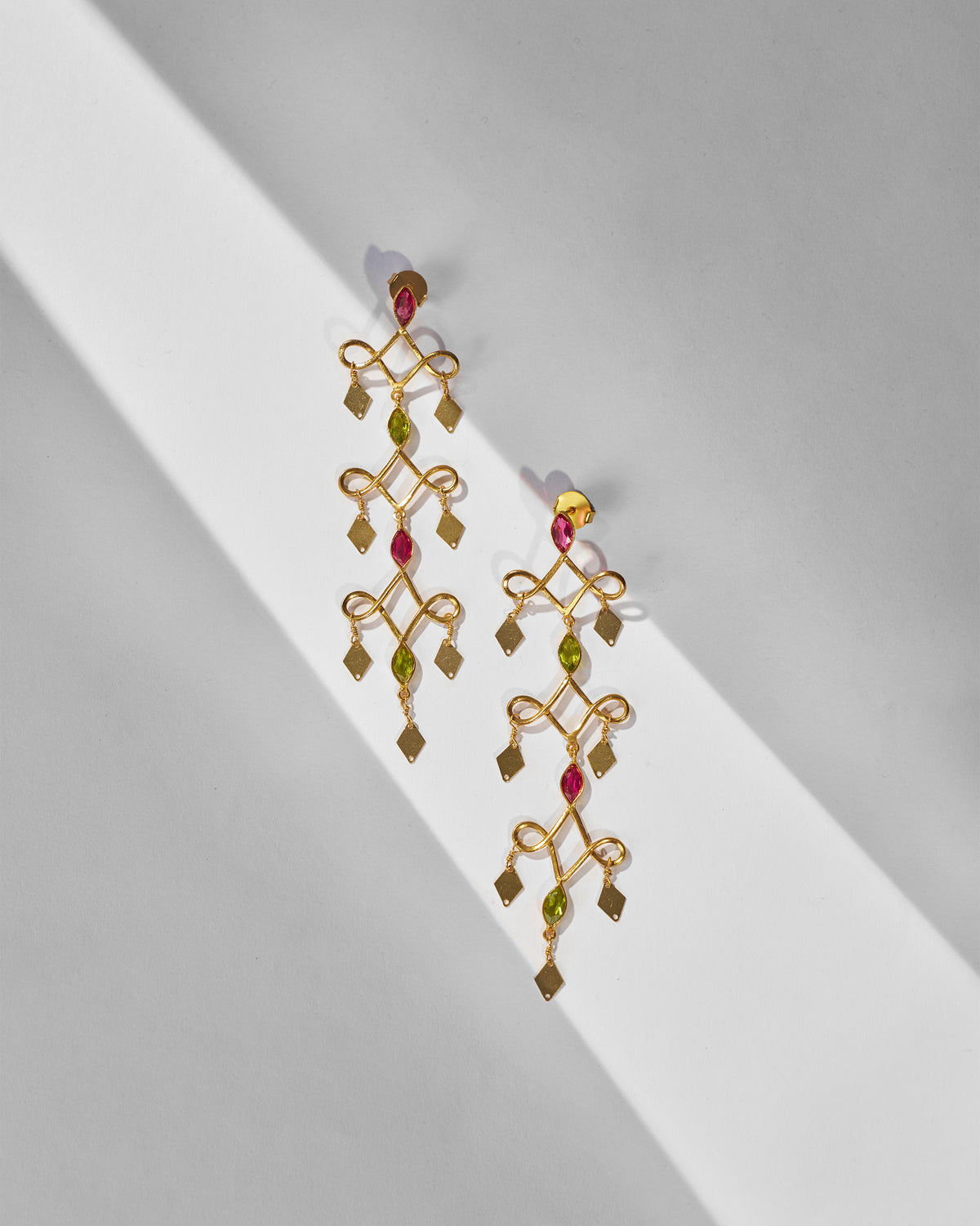 Pair of gold Kolam Danglers laid flat, showing pink and green stones.