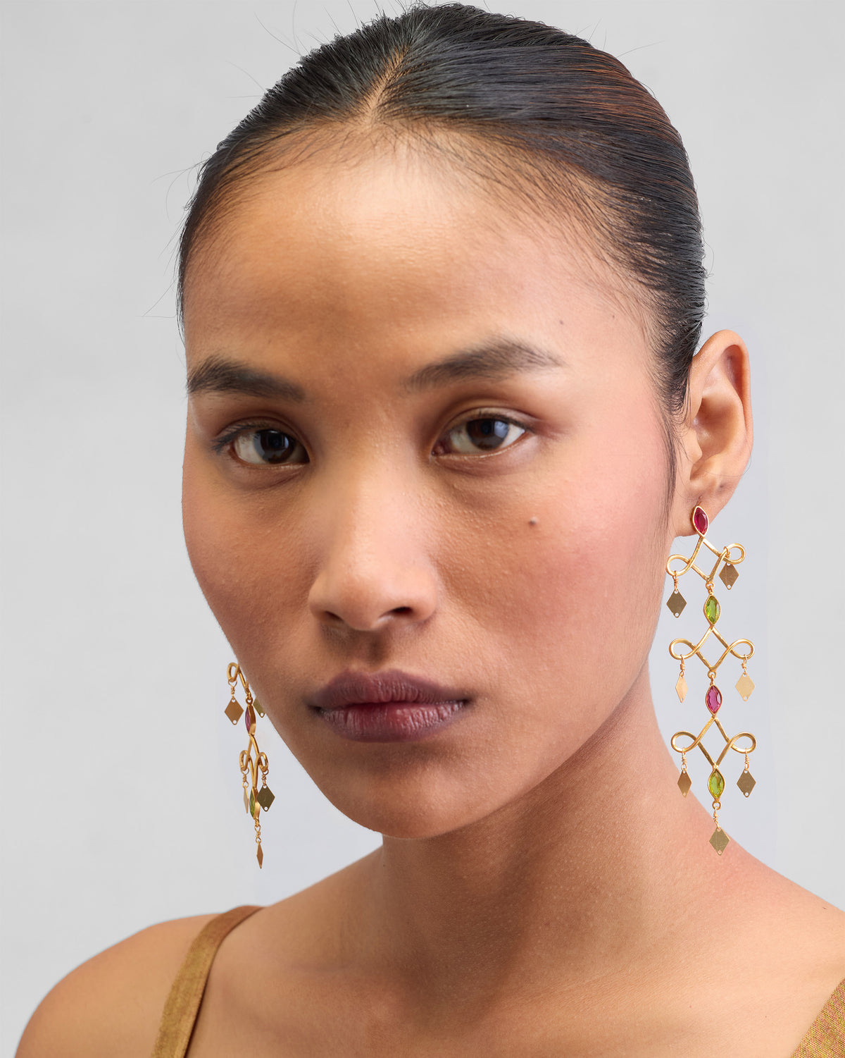 Person wearing gold Kolam Danglers with pink and green stones.