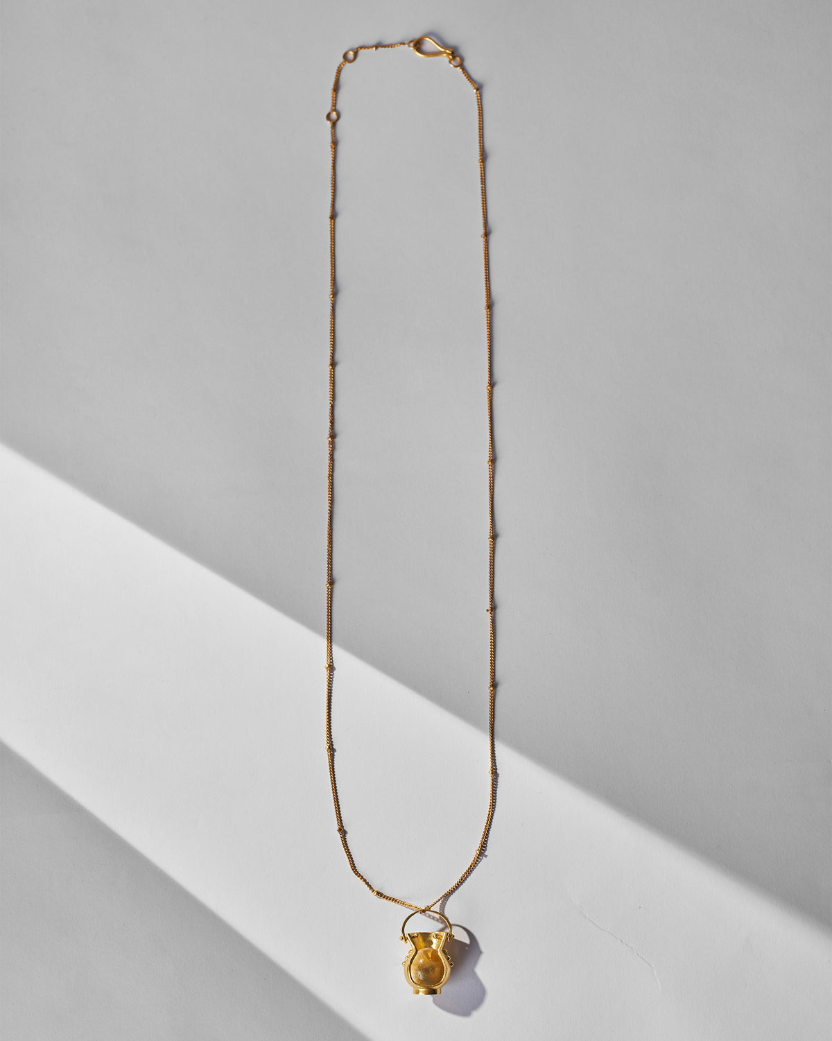 Long gold Sage necklace with a small pot pendant laid flat.