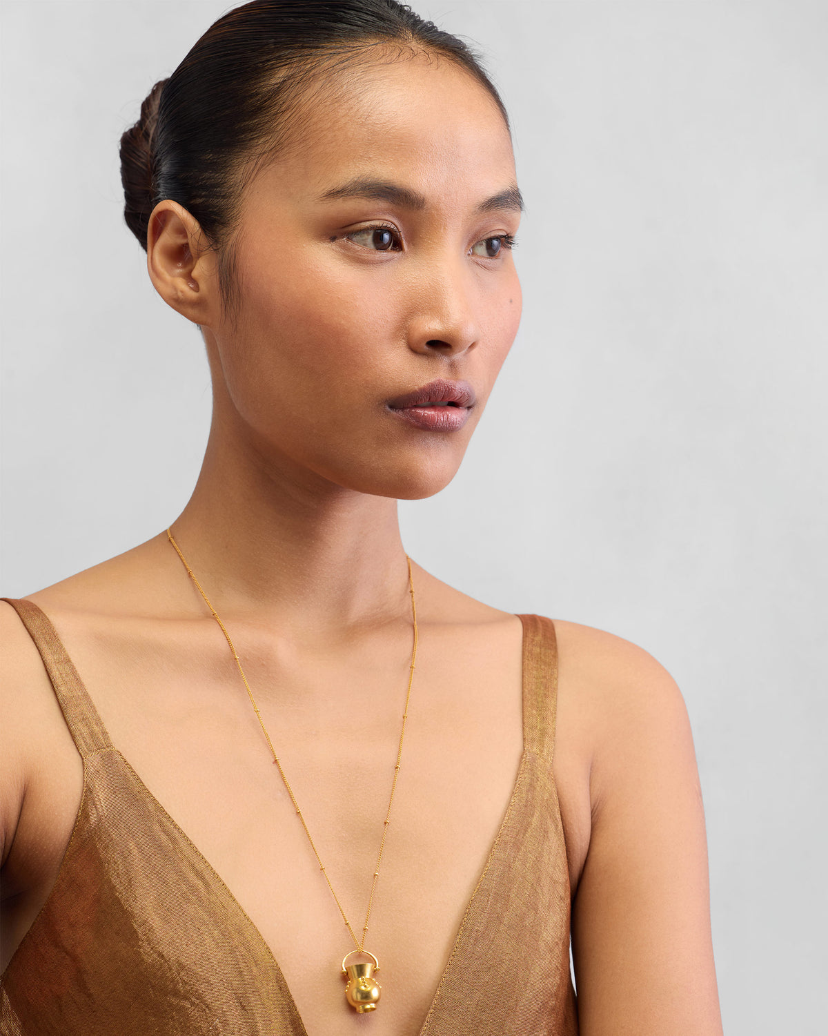 Person wearing a gold Sage necklace with a pot pendant.