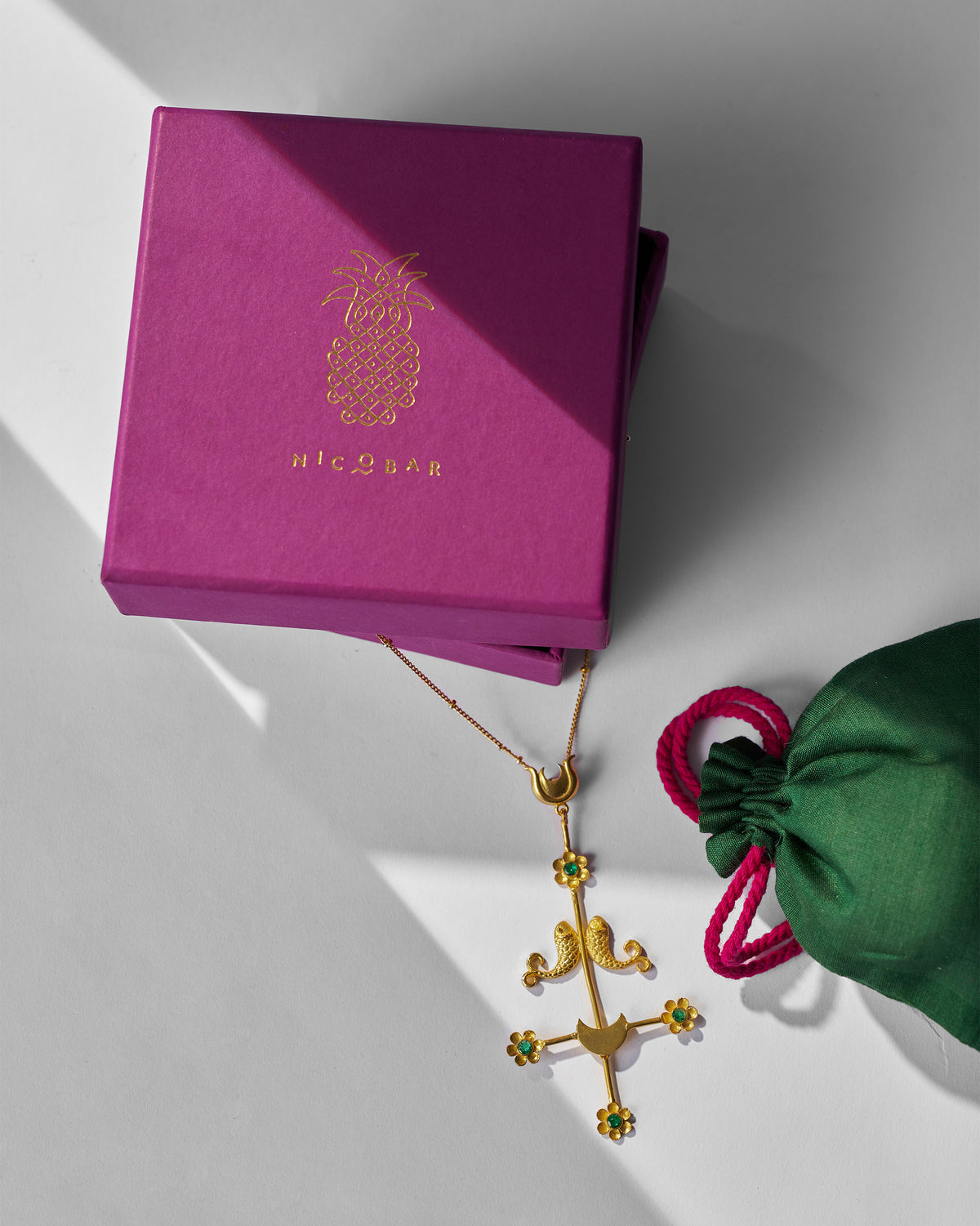 Gold Gul Baag necklace beside a magenta Nicobar box and green pouch.