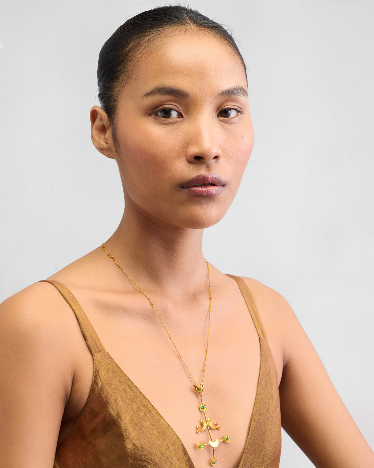 Person wearing a gold Gul Baag necklace with green flower stones on a V-neck.