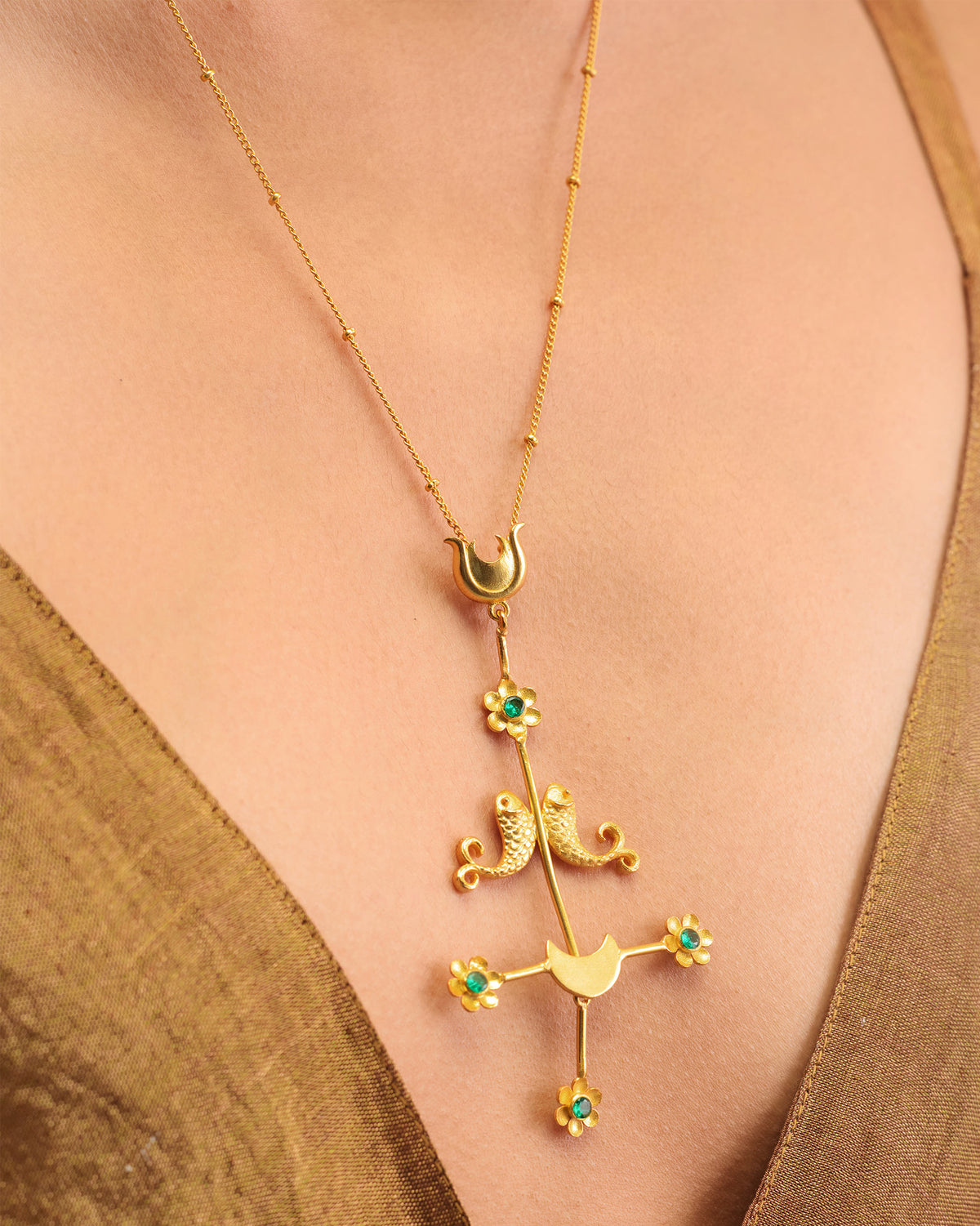 Close-up of the gold Gul Baag pendant with fish motifs and green stone flowers.