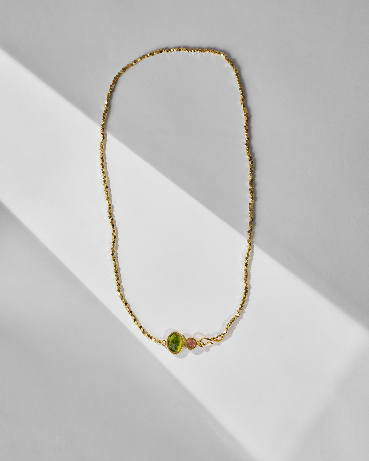 Gold Kari necklace with green and pink stones laid flat.