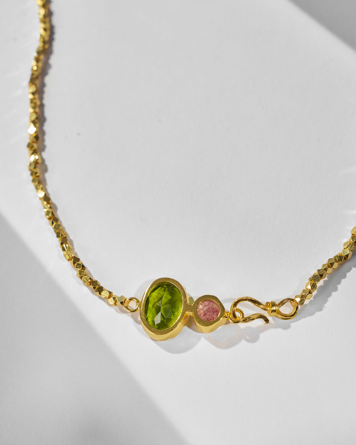 Close-up of a gold Kari necklace showing green and pink stones and clasp.