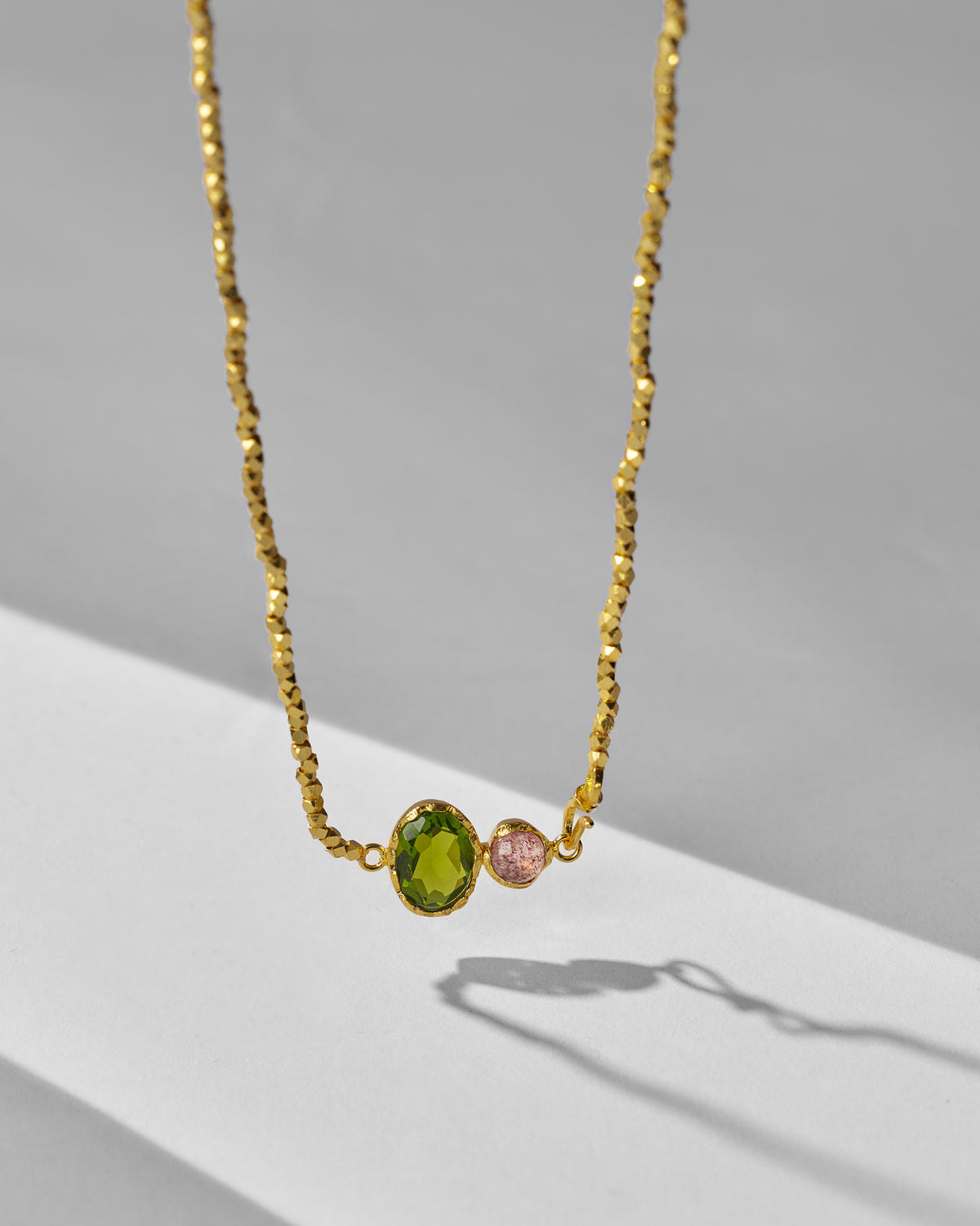 Close-up of a gold Kari necklace pendant with green and pink stones.