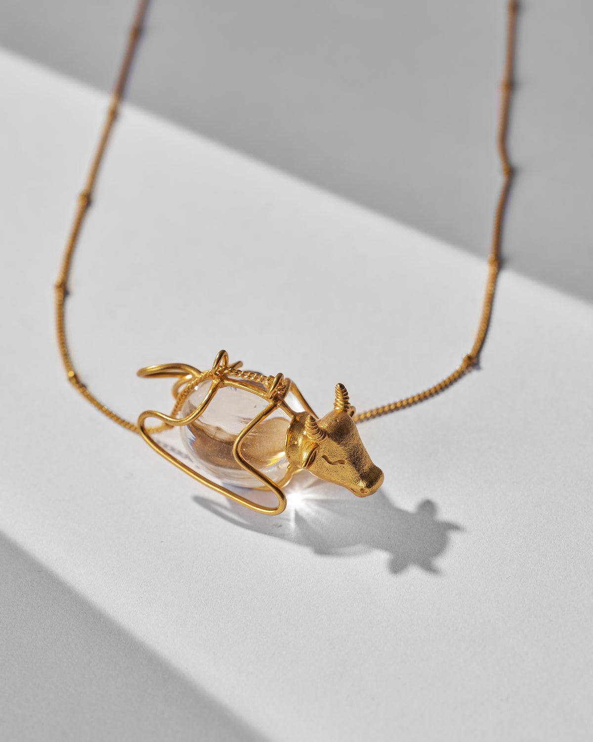Gold Nandi bull pendant with a clear oval body in a wire cage.