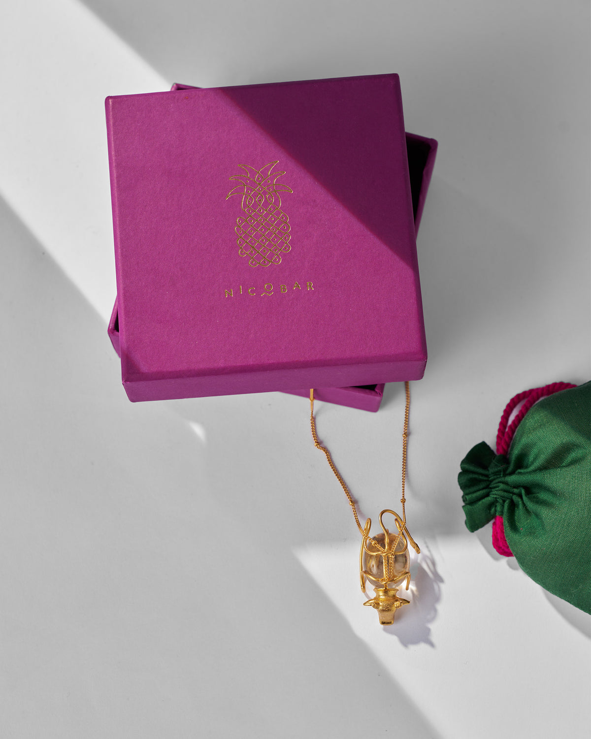 Gold Nandi necklace with clear pendant on a magenta Nicobar gift box.