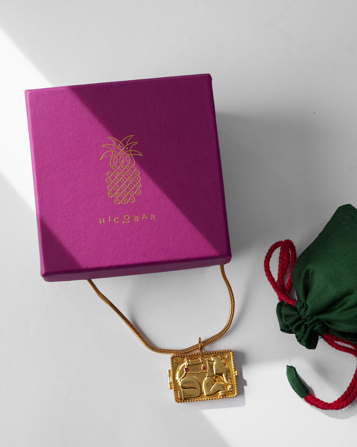 Gold Appu elephant locket necklace beside a magenta Nicobar gift box.