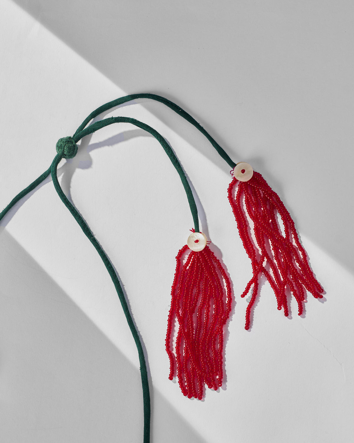Close-up of Phool Jaal necklace green cord ends with red beaded tassels.