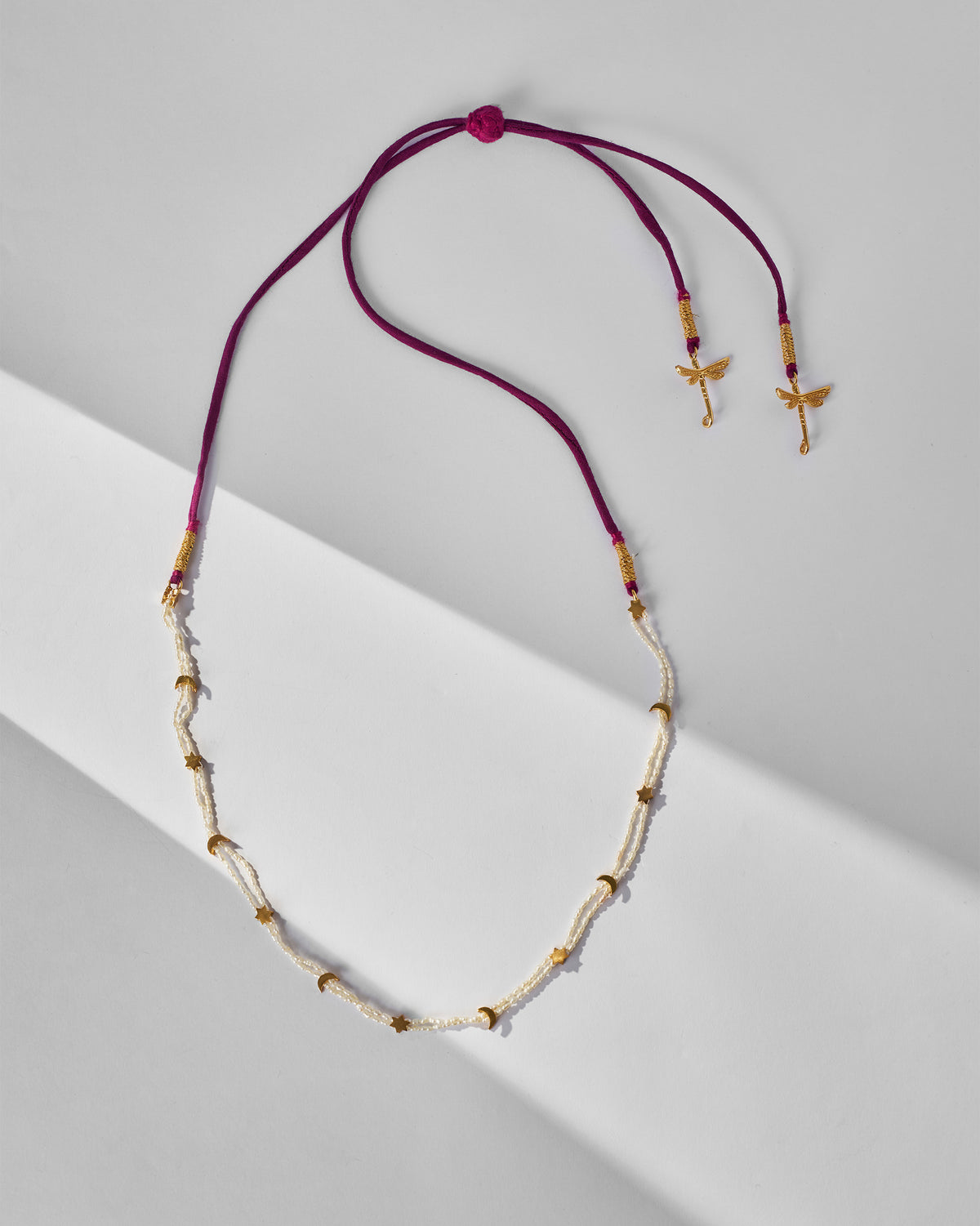 Bindu pearl necklace laid flat with magenta cord and gold dragonfly ends.