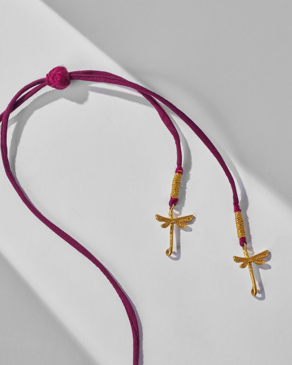 Close-up of magenta cord ends with gold dragonfly charms on a Bindu necklace.