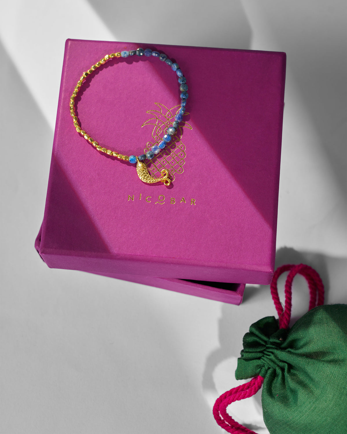 Jalpari Bracelet resting on a magenta gift box beside a green pouch.
