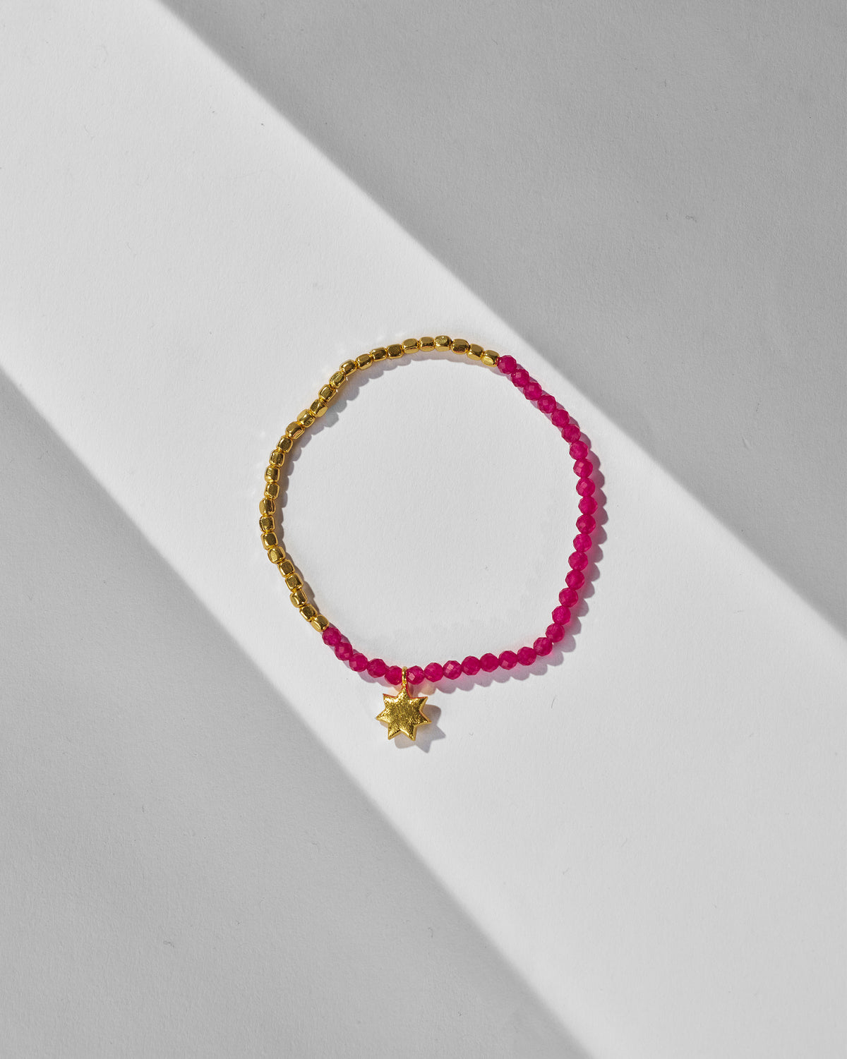 Pink and gold beaded Sitara Bracelet with a gold star charm, laid flat.