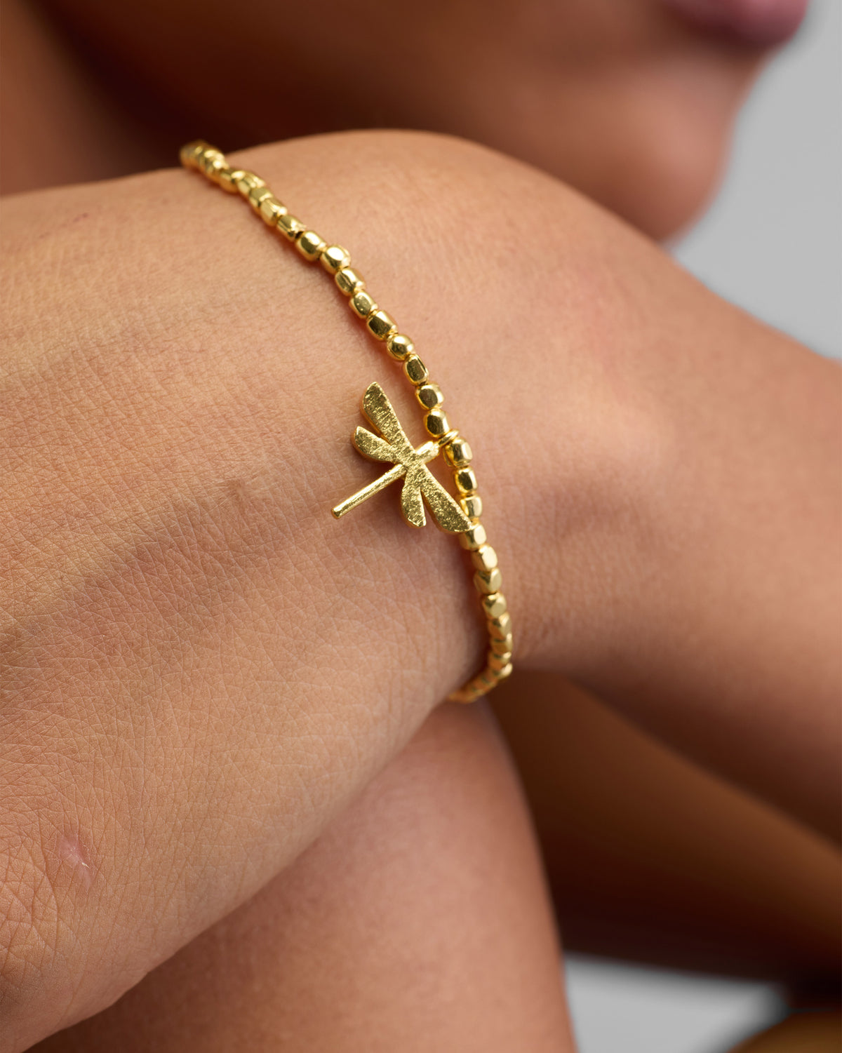 Close-up of a Dragonfly Bracelet on a wrist, showing its gold dragonfly charm.